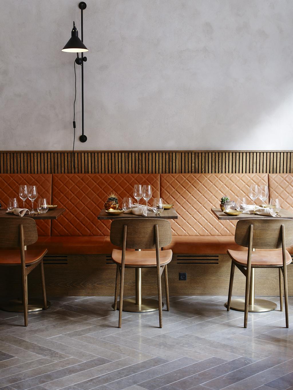 Gennemtænkt indretning med grå vægge og gulv, cognacfarver på quilted læder og sæde og træpaneler og træstole