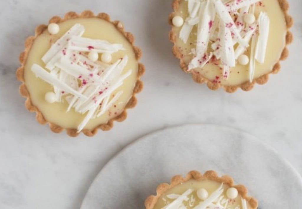 Mini-tærter med hindbær og hvid chokoladeganache, Pynt med hvide chokoladespåner, hvide chokoladeperler og hindbærpulver.