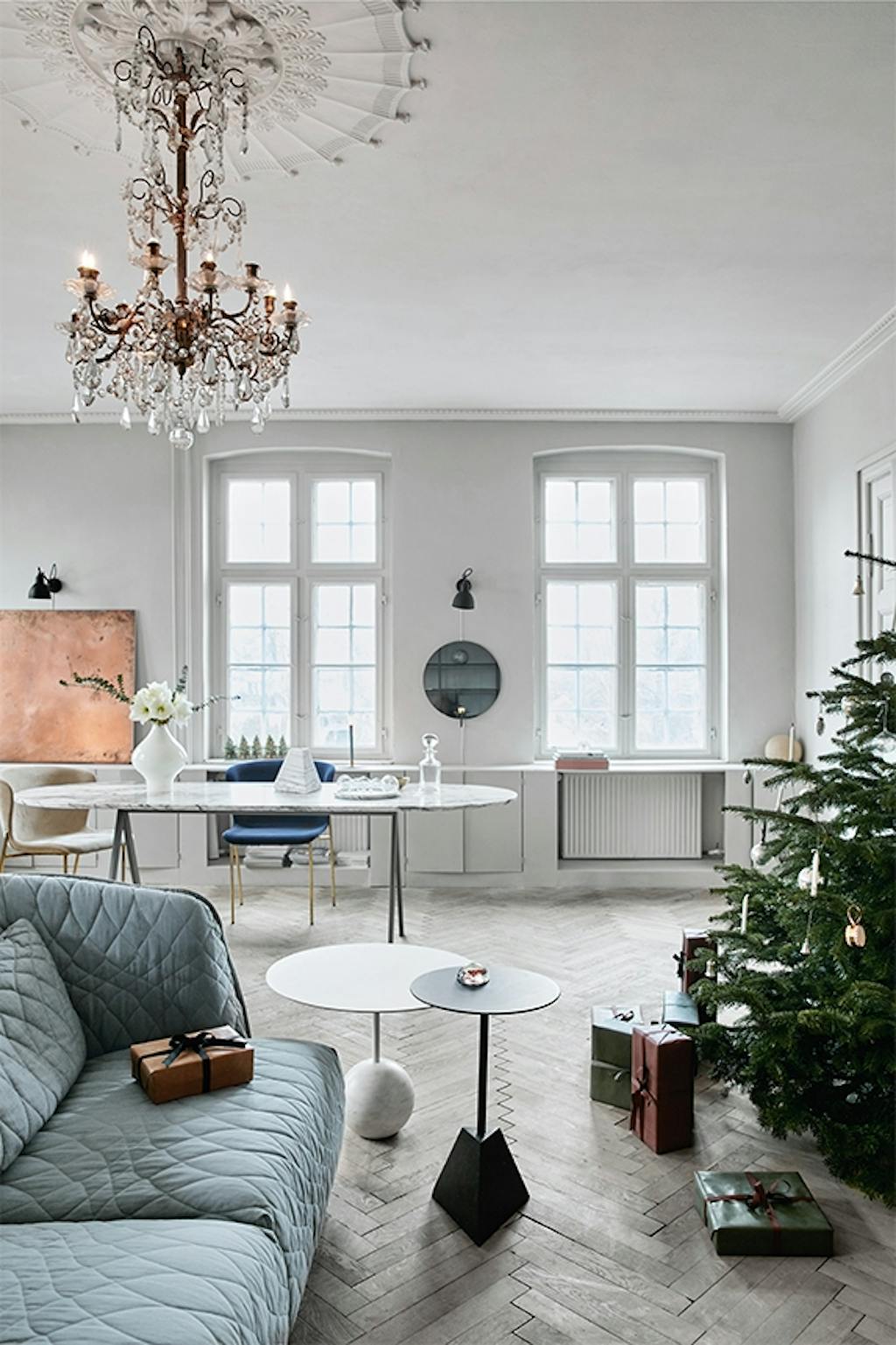 stue med stor lysekrone og grå sofa og juletræ