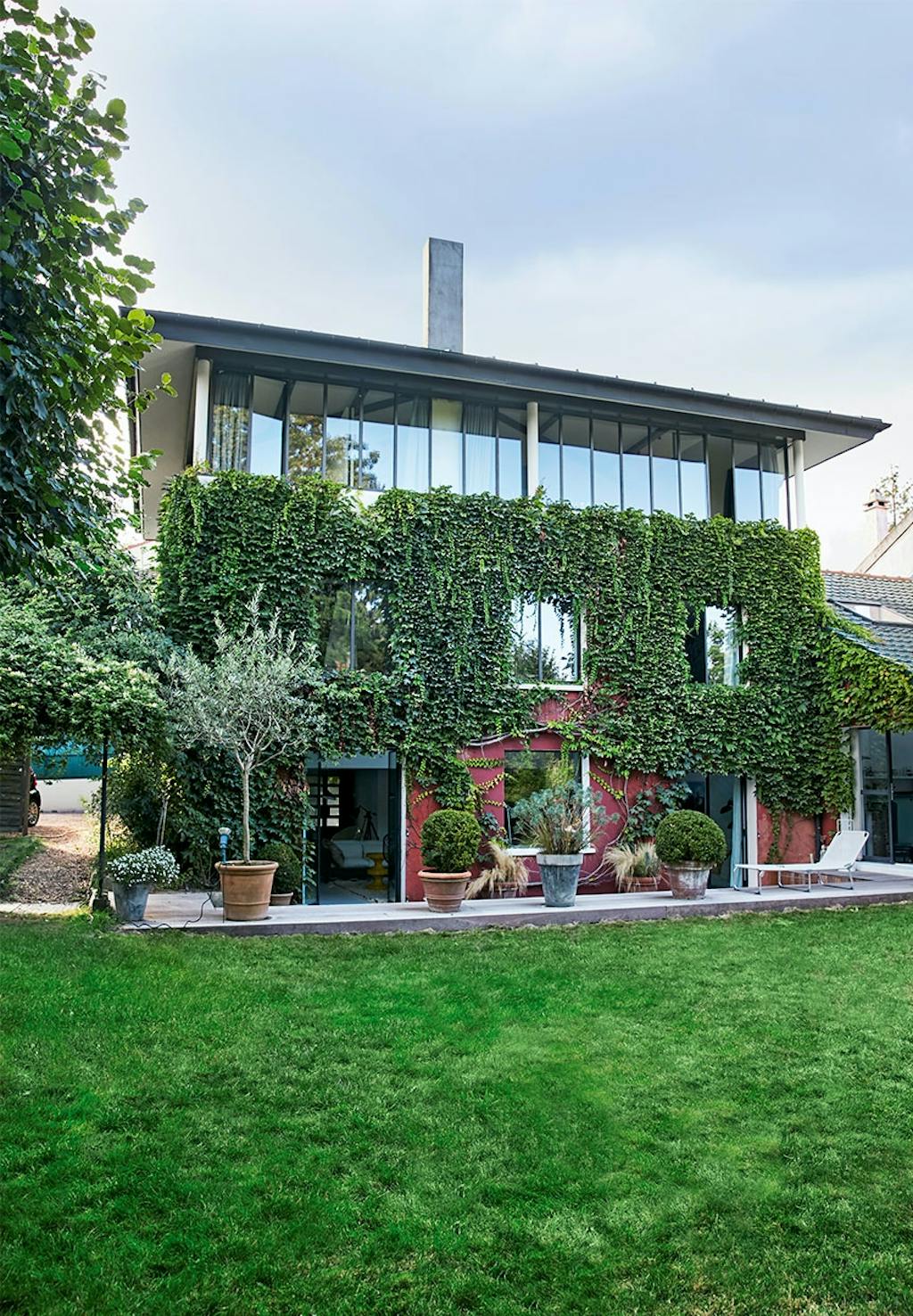 Facade af bagsiden af huset med terrasse, have, vedbend på facaden og øverste etage kun af glasvægge