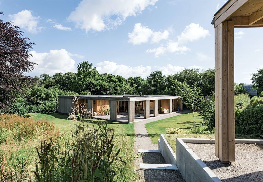 Udsigt over det kubeformede hus med have og lille skov til