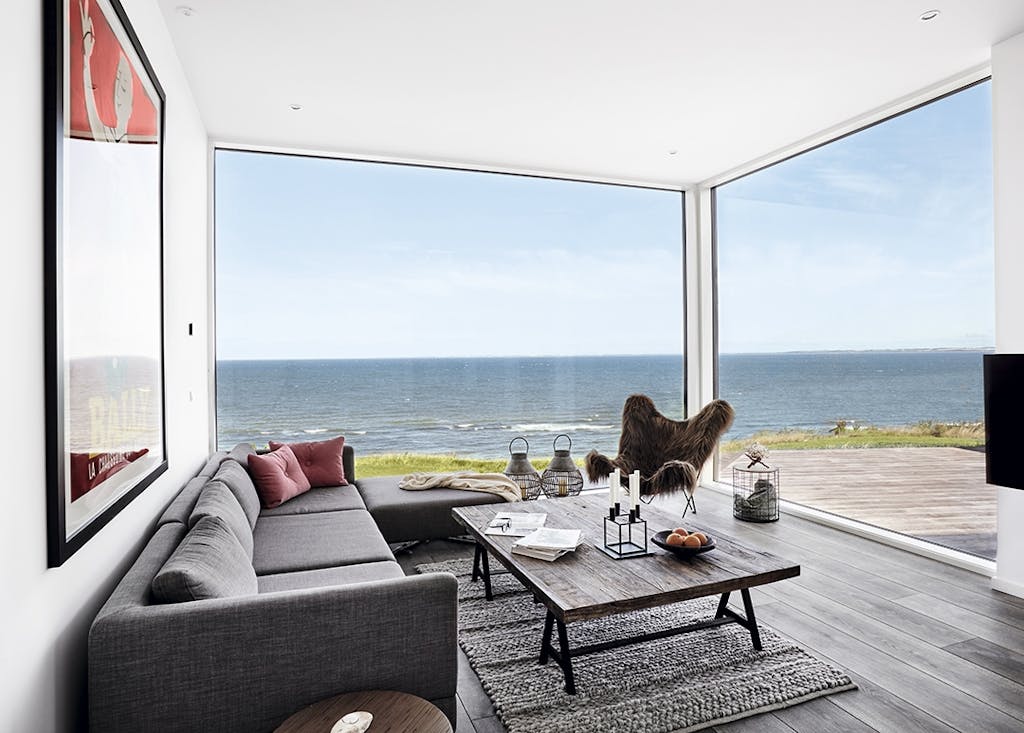 Opholdsstue med sofa og lænestol og udsigt udover havet Opholdsstue med sofa og lænestol og udsigt udover havet