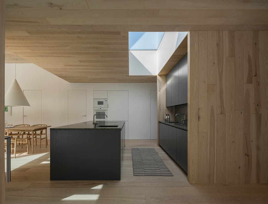 Køkken-alrum med mørkt køkken og træ