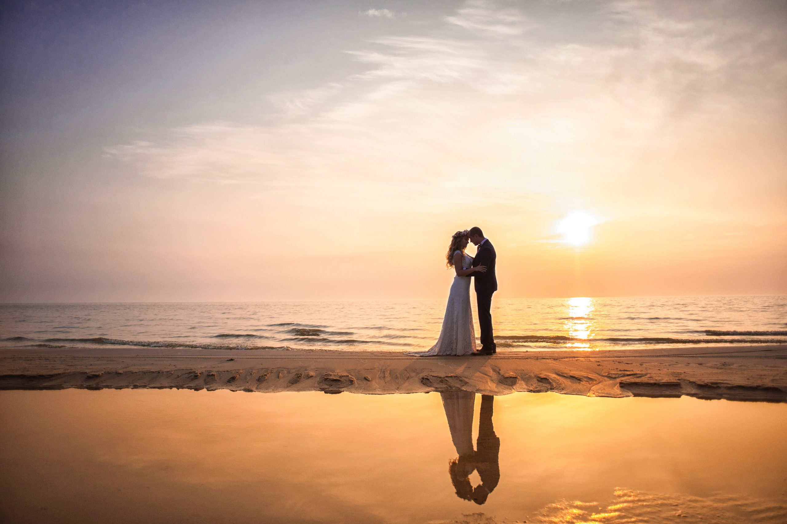 Hääpari rannalla auringonlaskua vasten