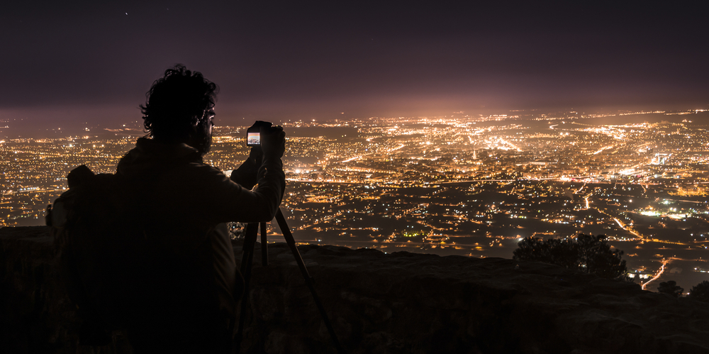 Fotograf stiller inn kameraet sitt før han tar et bilde av opplyst storby i natten