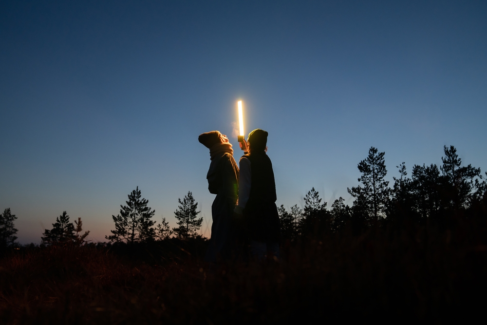 kaksi henkilöä pitää koholla valotikkua, joka valaisee heidän kasvonsa hämärässä 