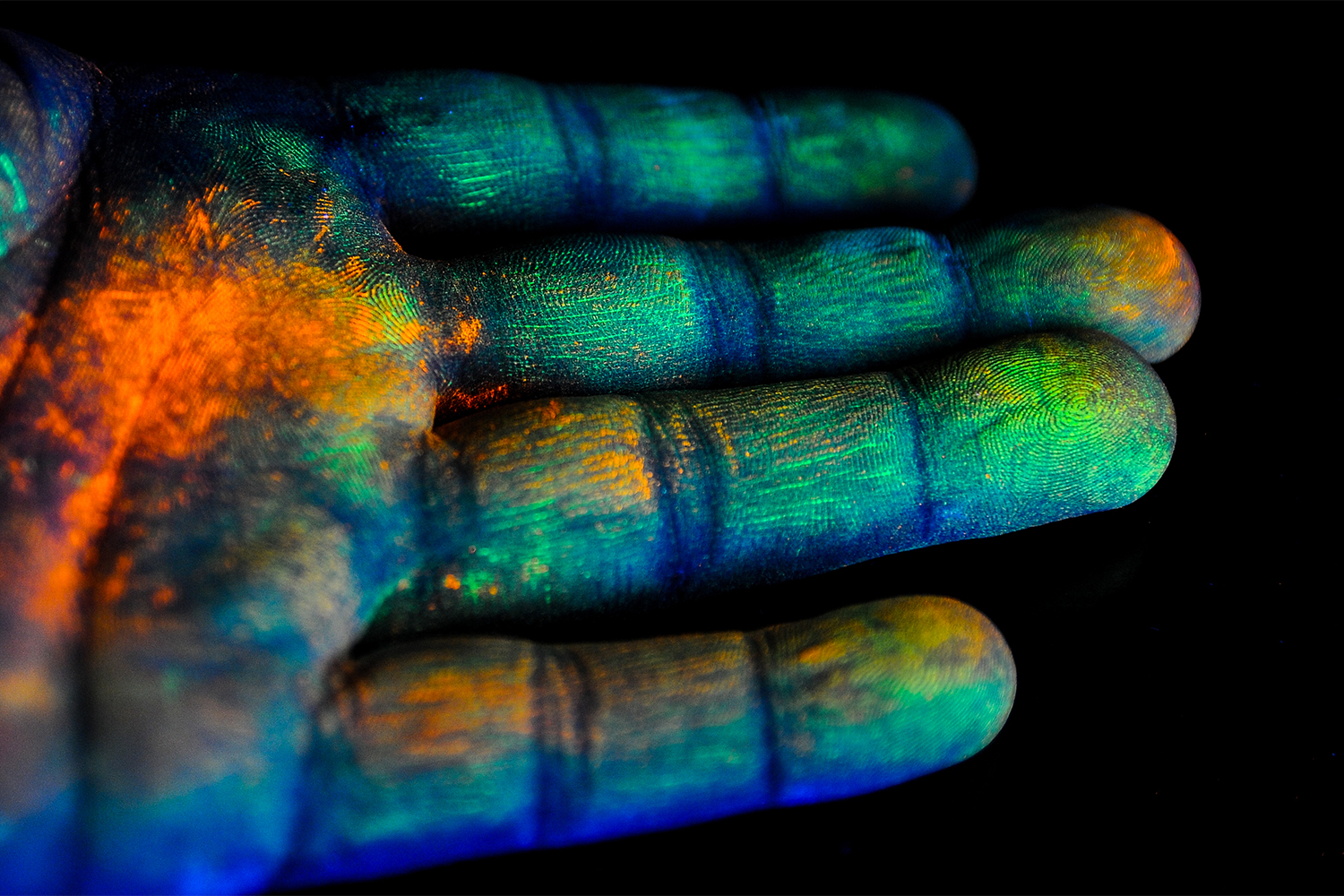 Oranssia ja vihreää jauhetta täynnä oleva käsi ojentuu kohti kameraa mustalla taustalla