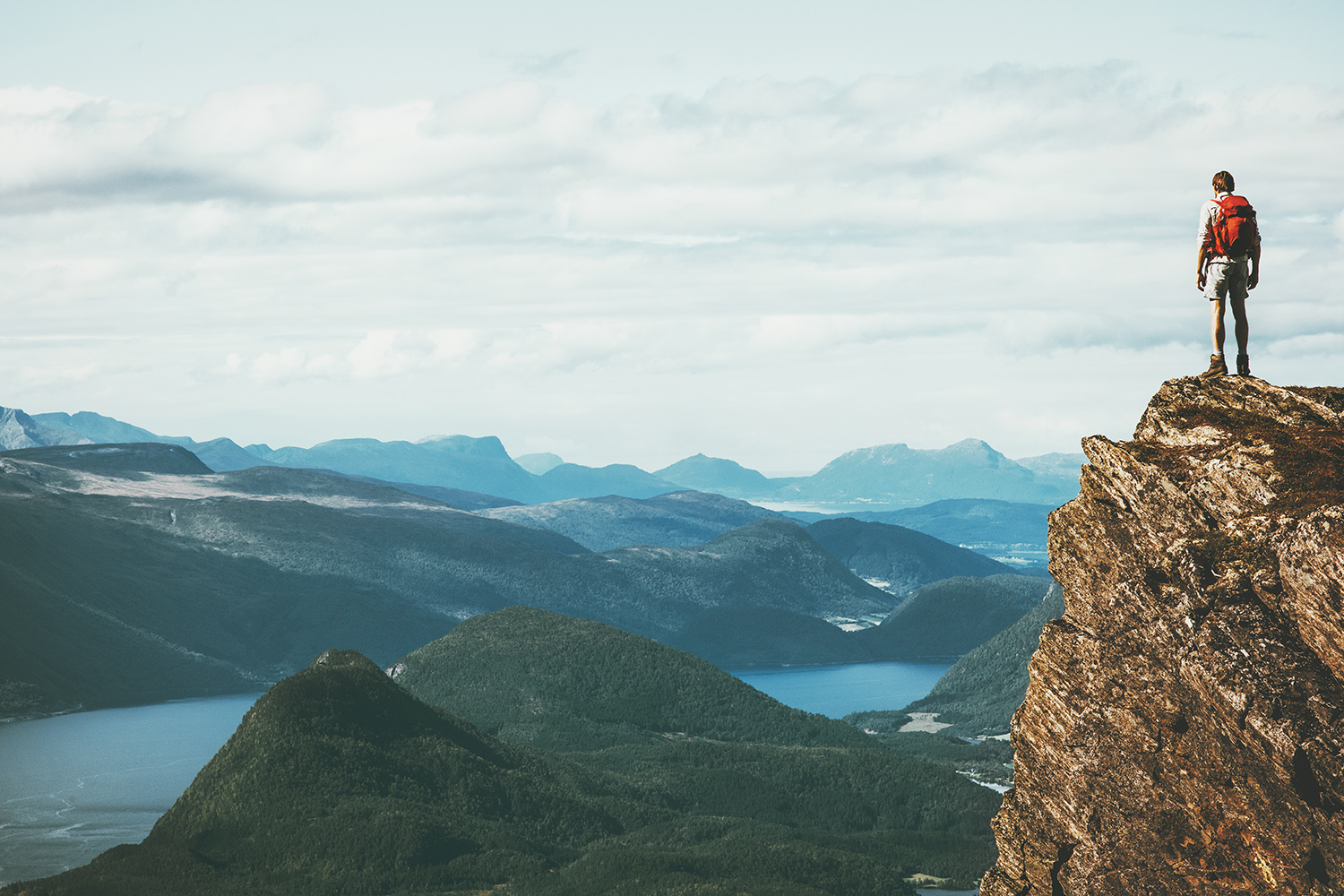 Landskapsfoto, man på hög klippa med berg i bakgrunden
