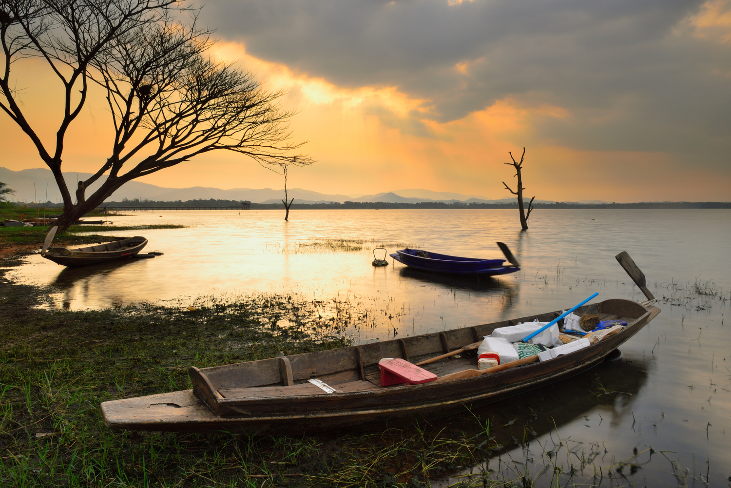 Båt ligger i vannkanten mens sola går ned