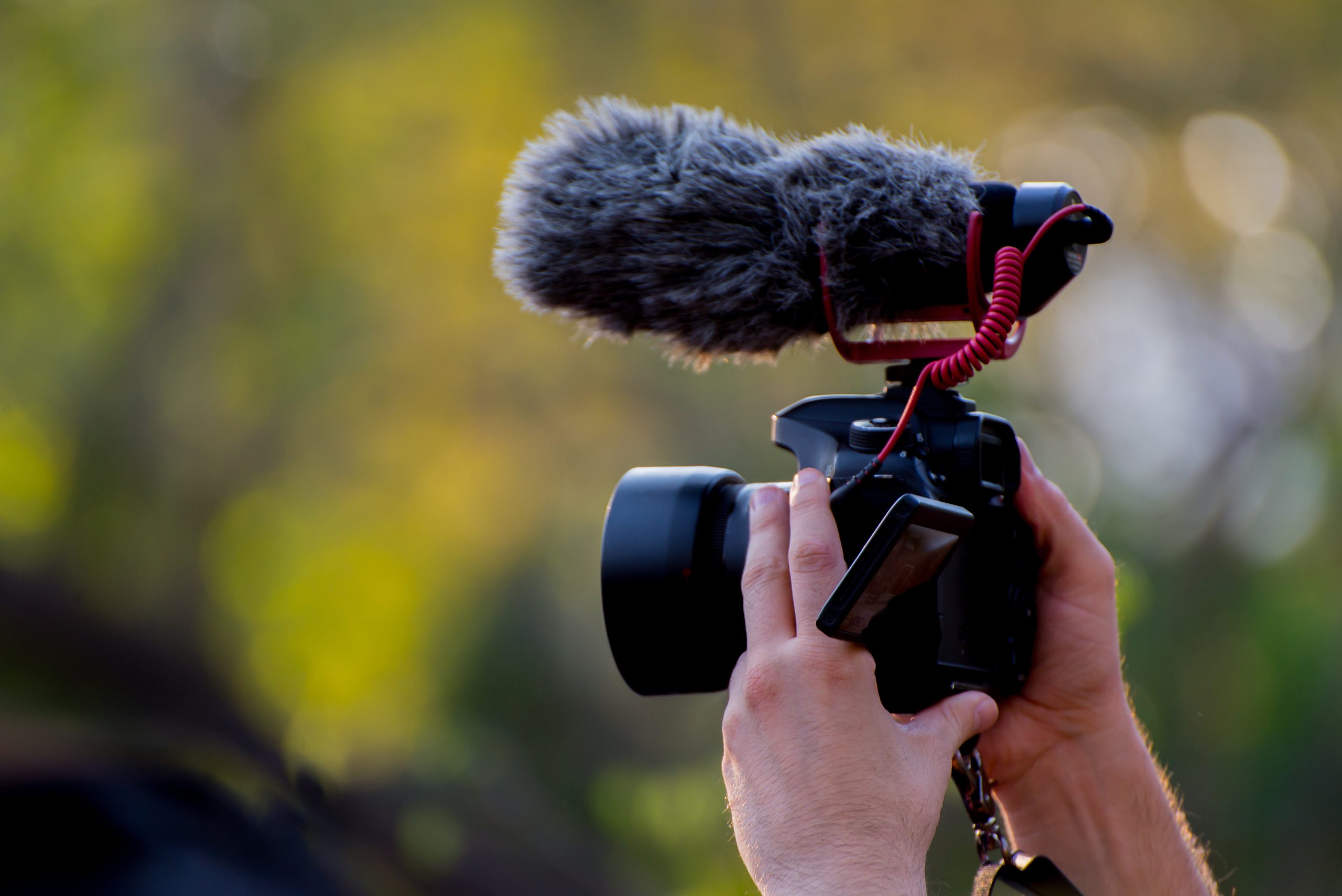 Händer håller en kamera med en mikrofon monterad ovanpå 