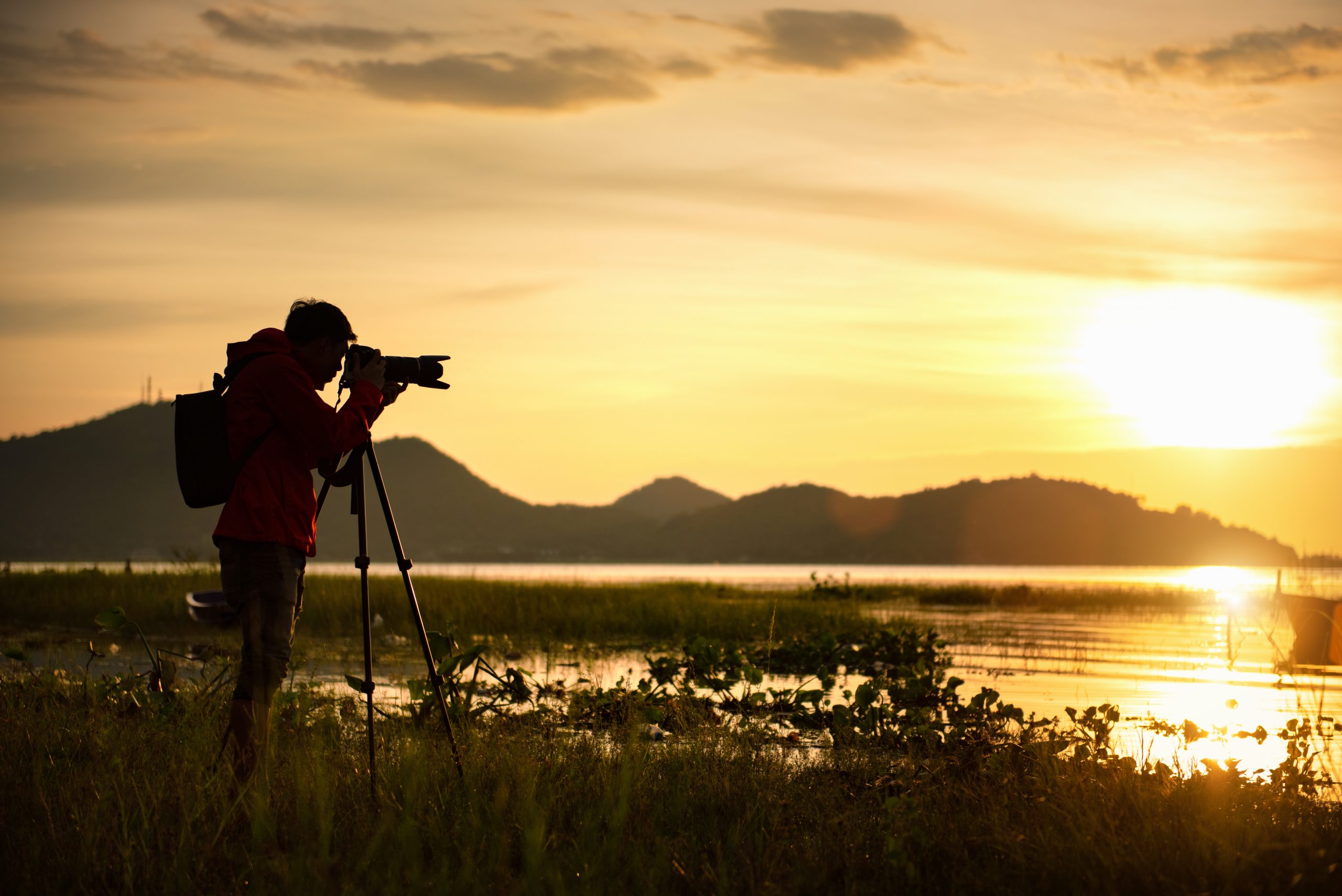 Man fotograferar solnedgången med kamera och stativ