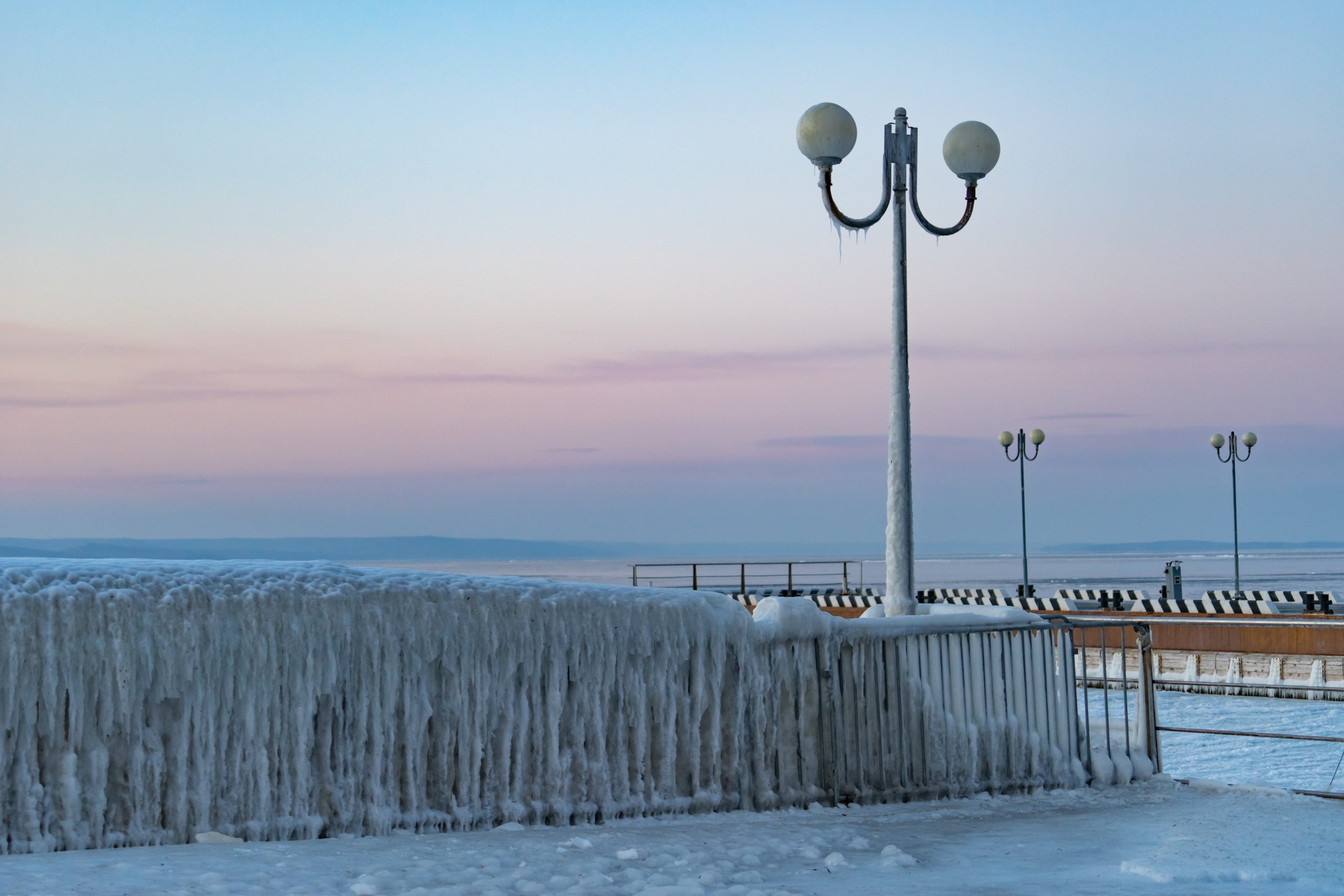 Isbildning på räcken och lyktstolpar vid kusten i solnedgång