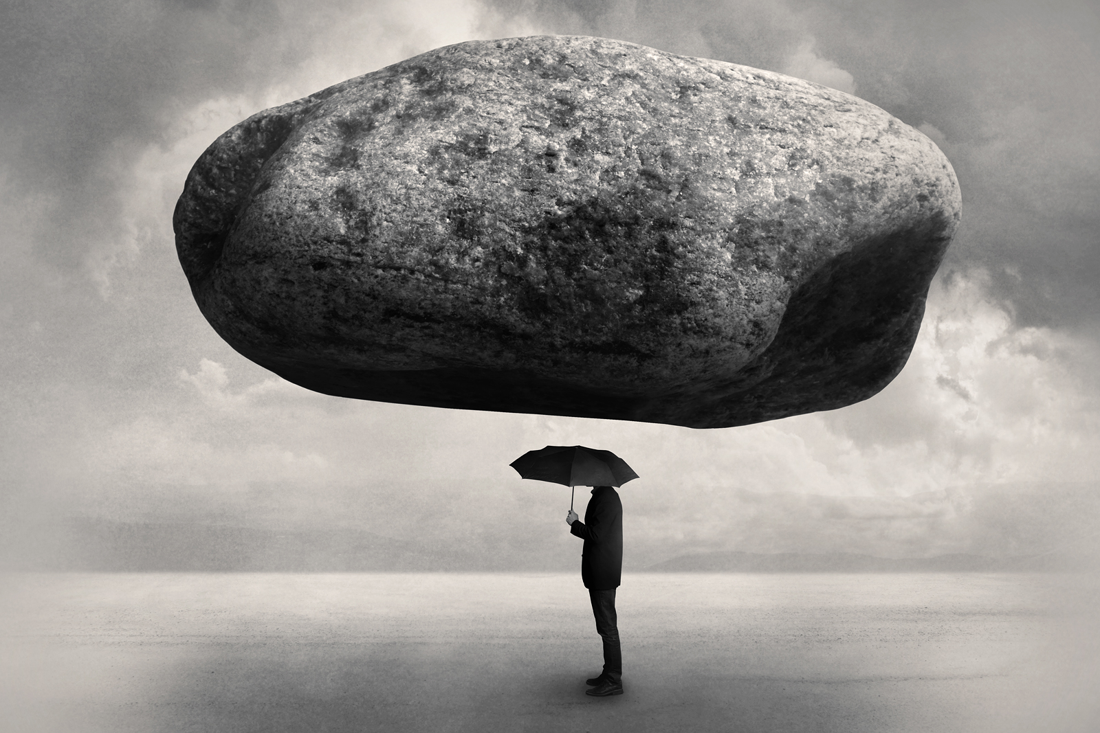 Man i kostym med paraply under stor sten