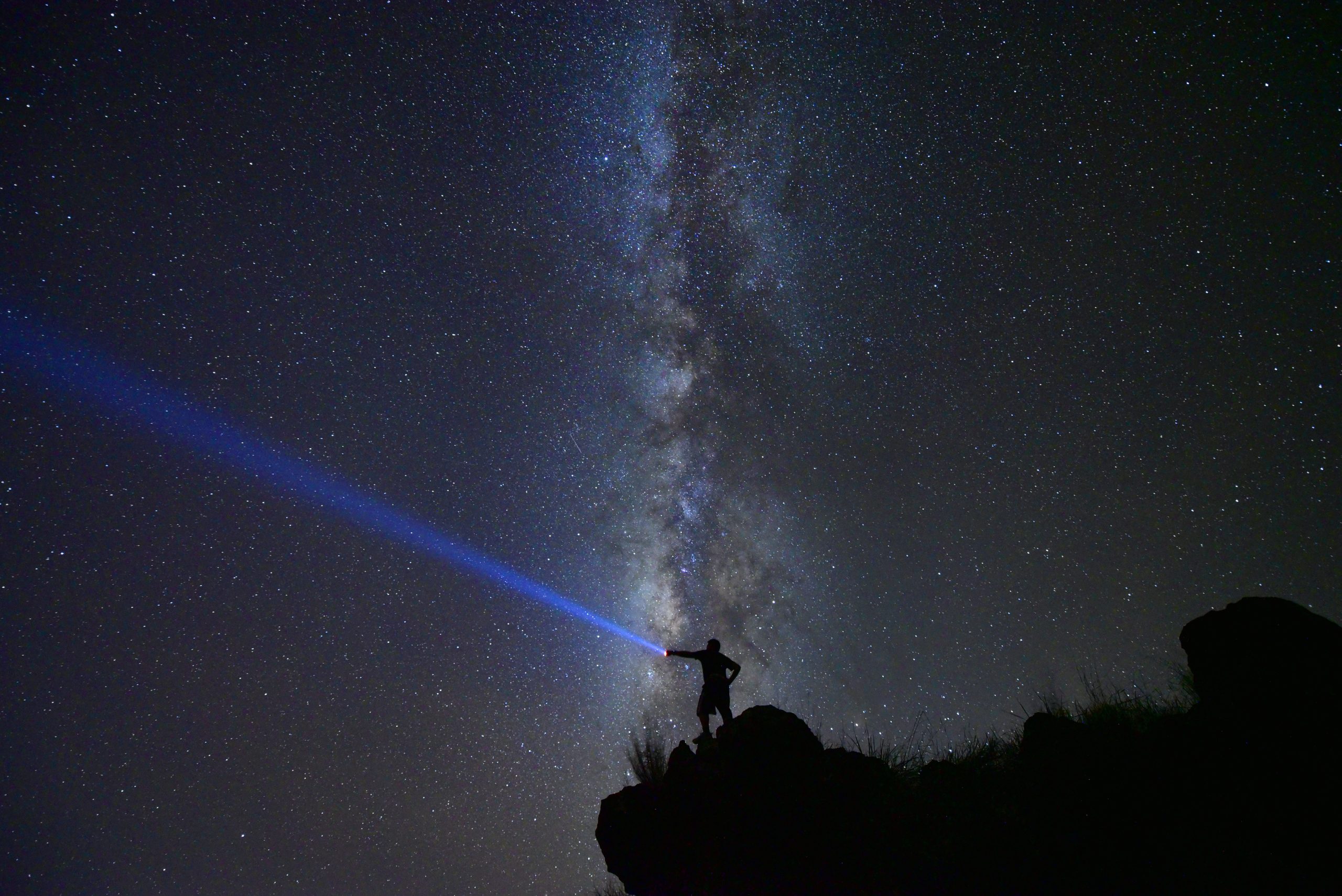 Person med ficklampa framför himmel med Vintergatan