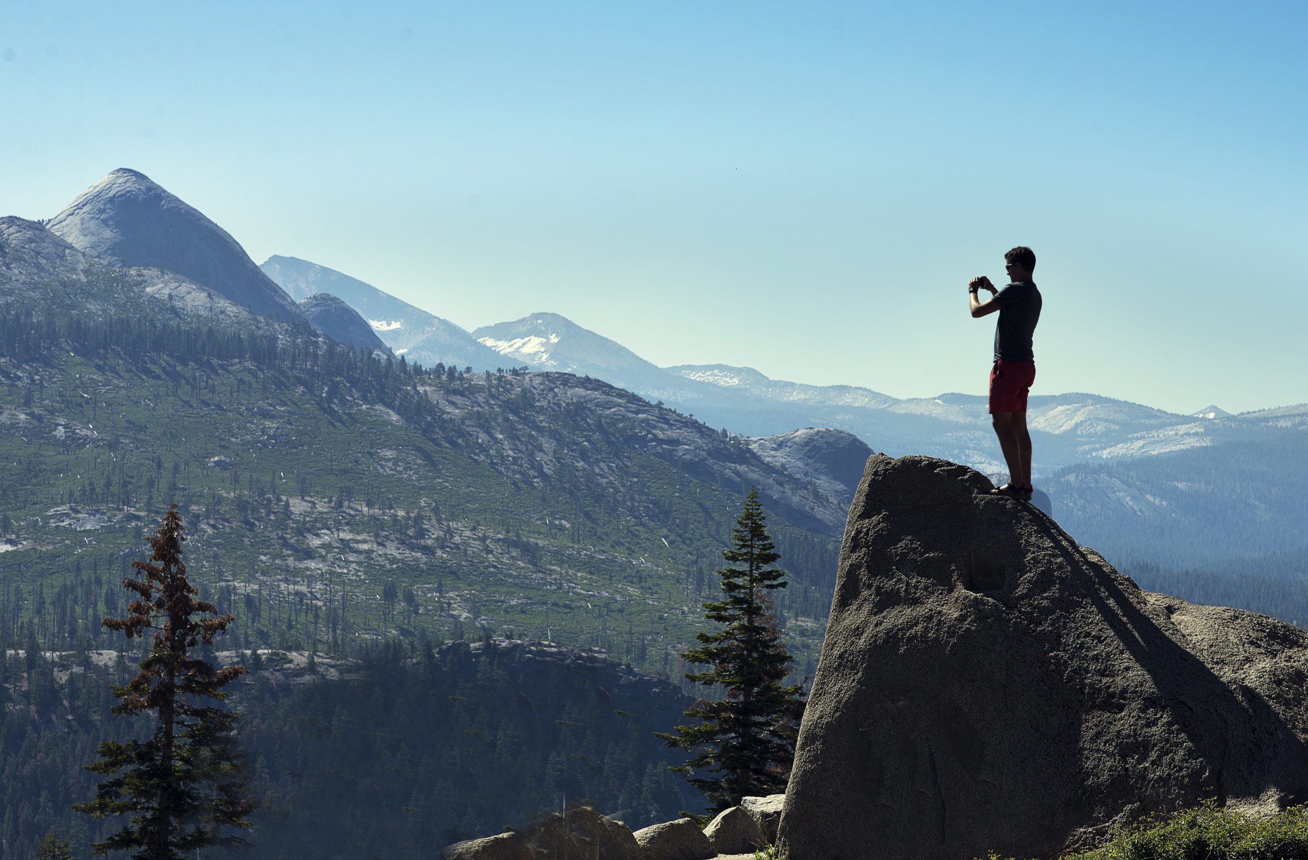 Mand står på bjergtinde og fotograferer med sin telefon