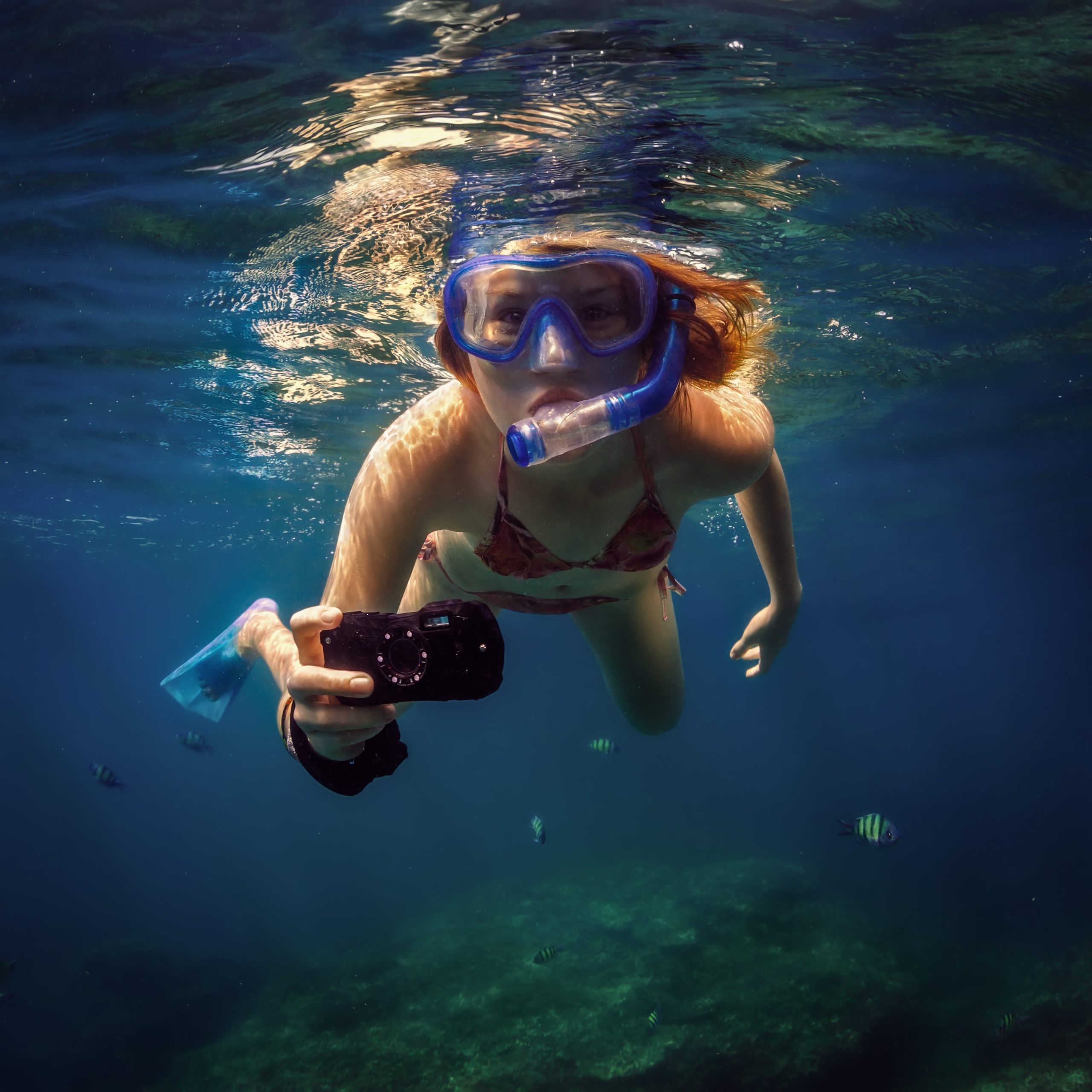 Kvinde snorkler med et undervandskamera i hånden.