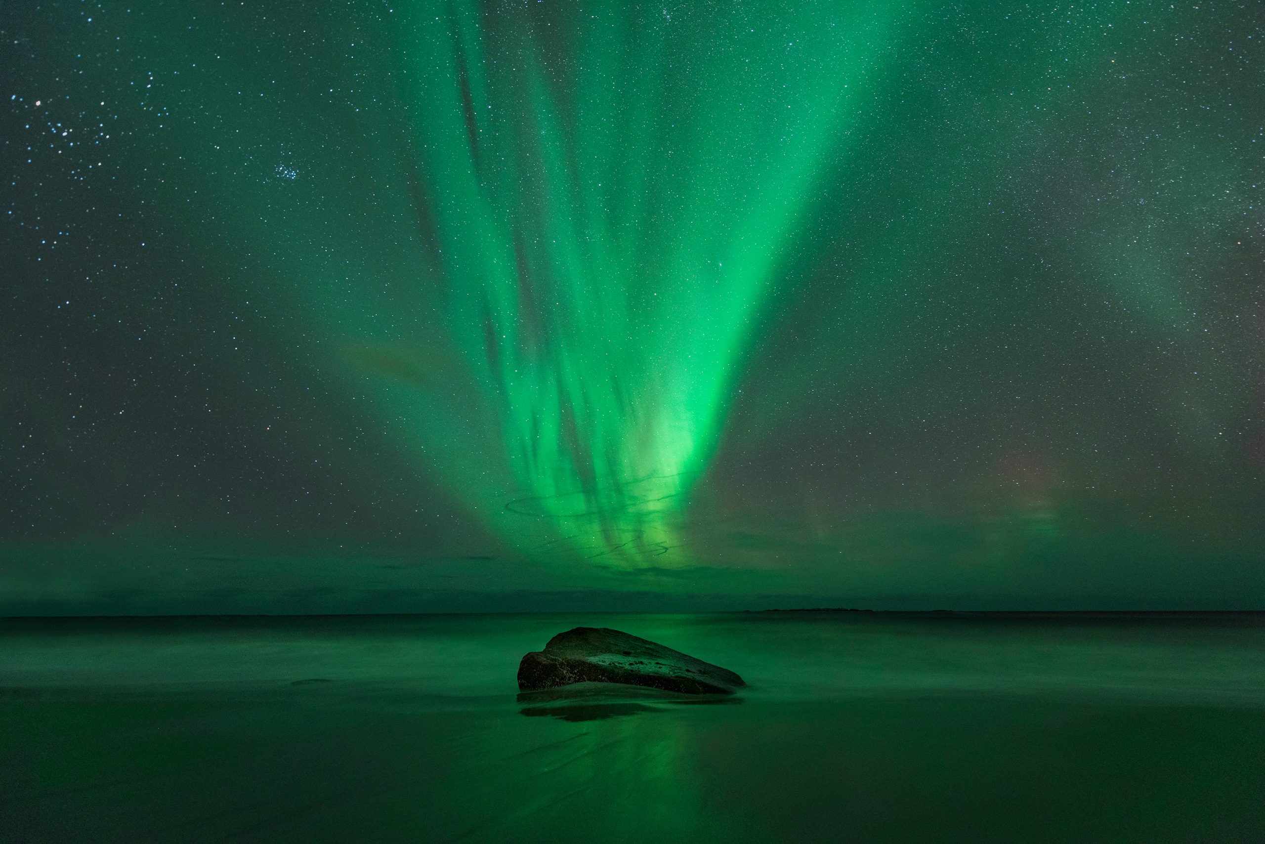 Nordlys over hav med sten i forgrunden