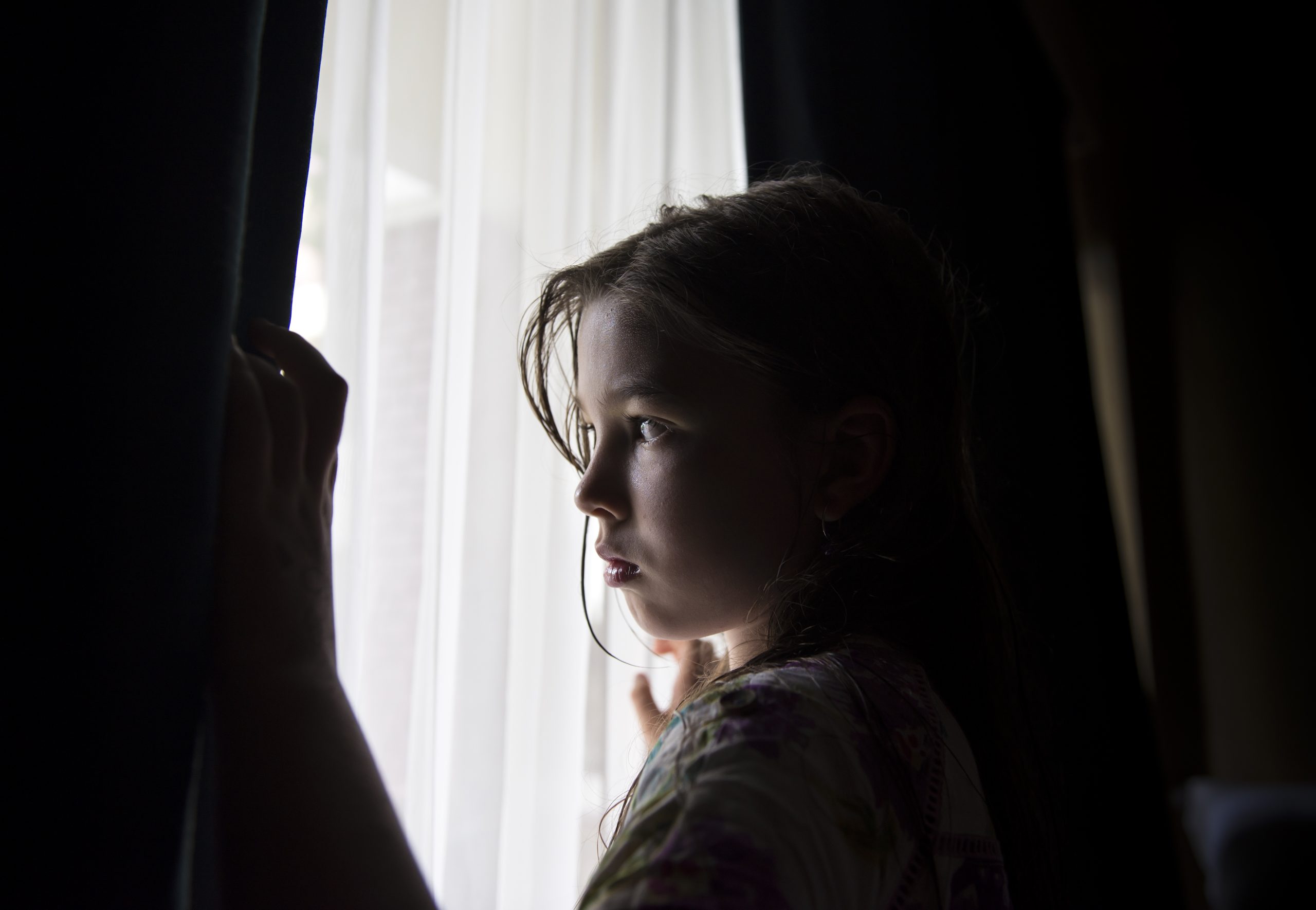 Liten jente trekker fra  gardiner og ser ut av vindu