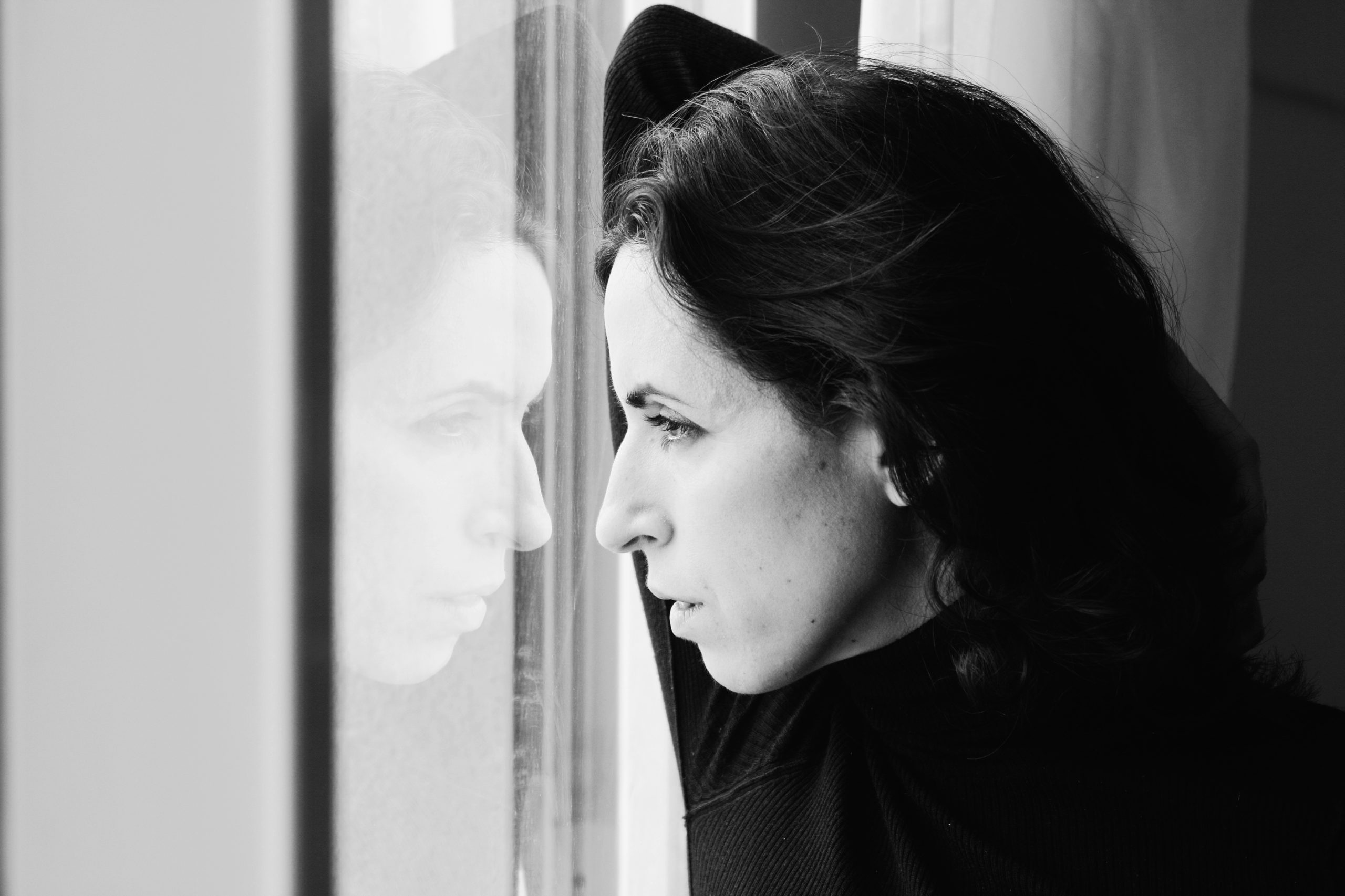Ung kvinde i profil kigger ud af et vindue i sort-hvid