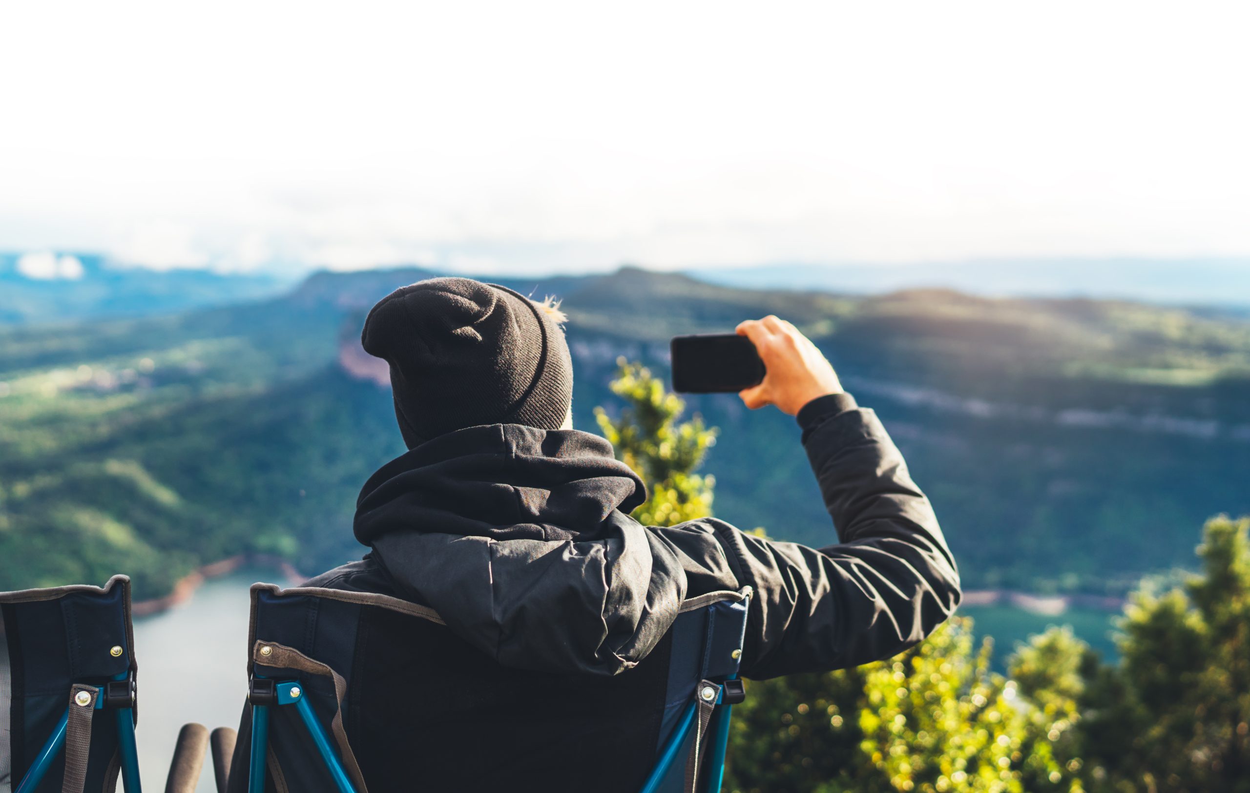 Mann sitter i campingstol og tar bilder med mobilen