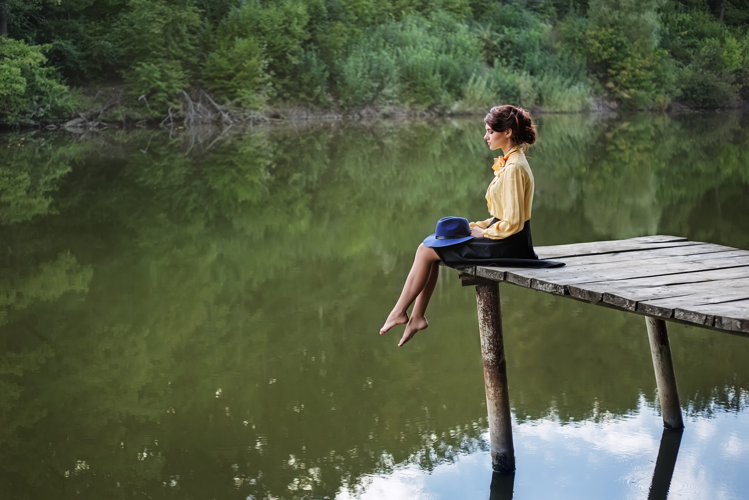 Ung kvinne som sitter på en brygge i et vakkert landskap