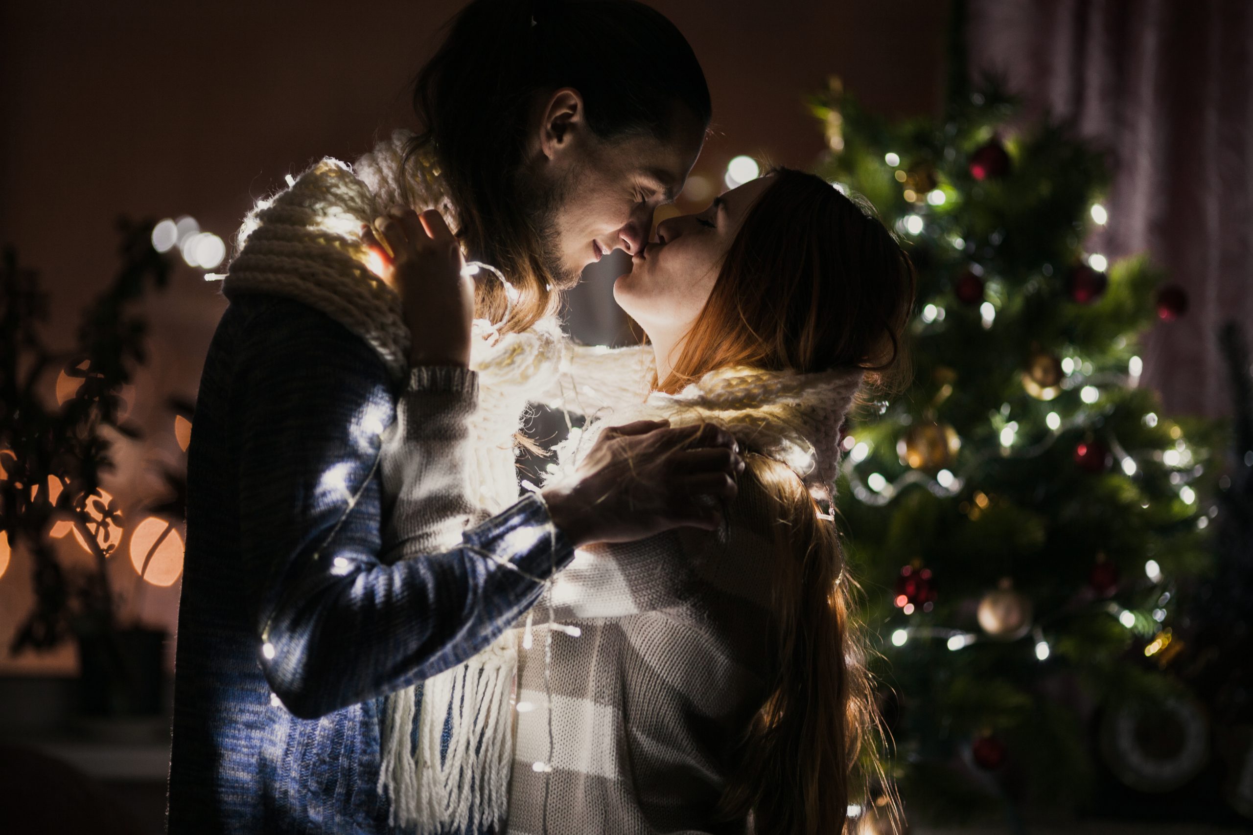 Ungt par kysser ved juletræ