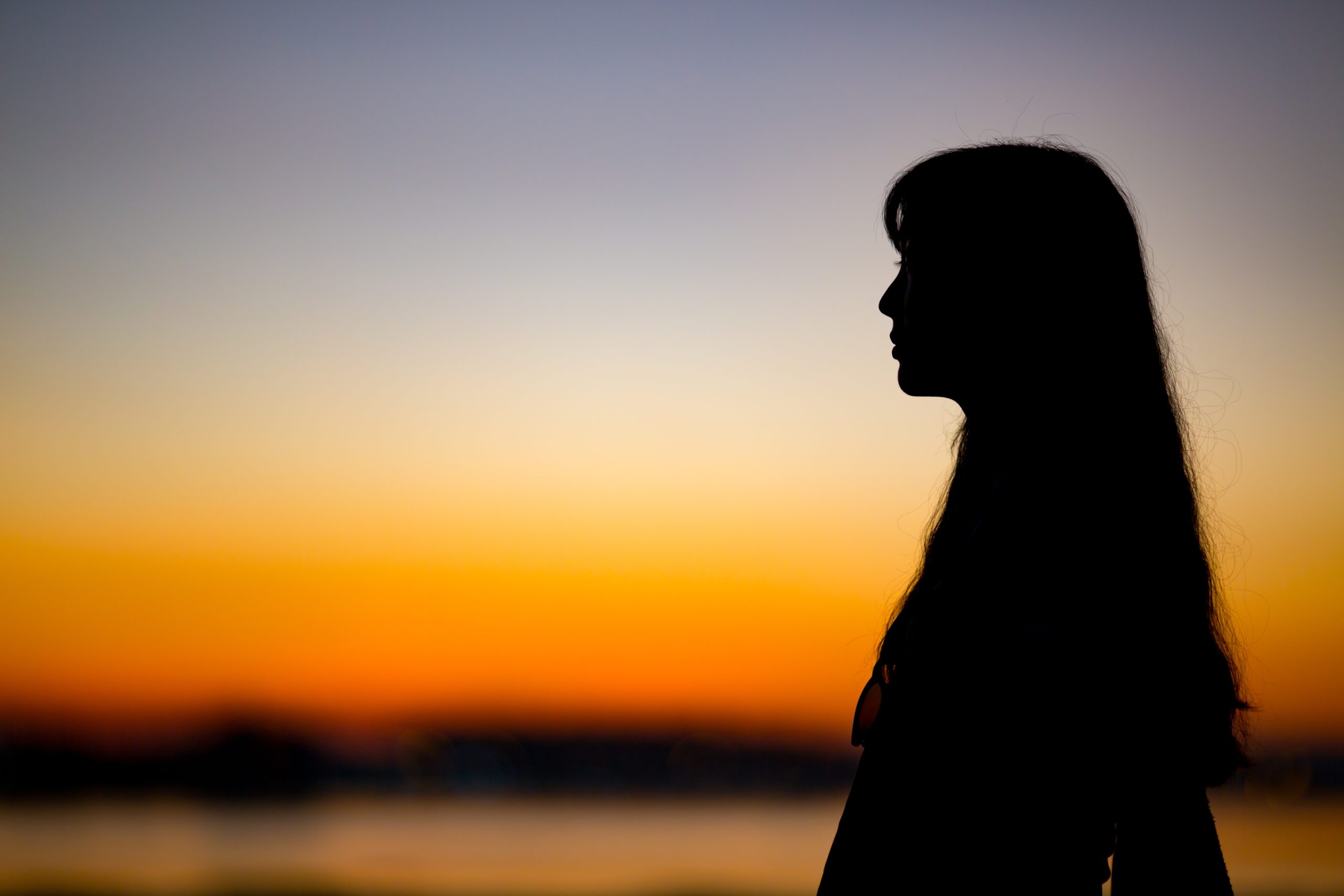 Silhuet af kvinde med siden til i solnedgang