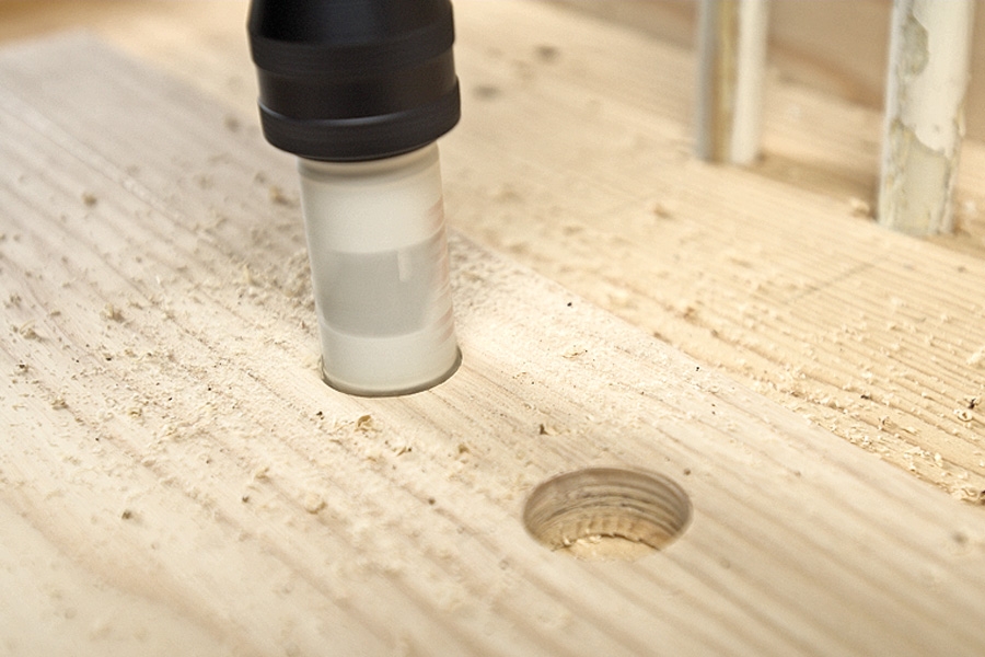 Ilappning mellan två längsgående golvbrädor: Brädorna sätts ihop långsida mot långsida, och hålen borras med en hålsåg – 10 mm större än rörens diameter, så det är luft runt om rören.