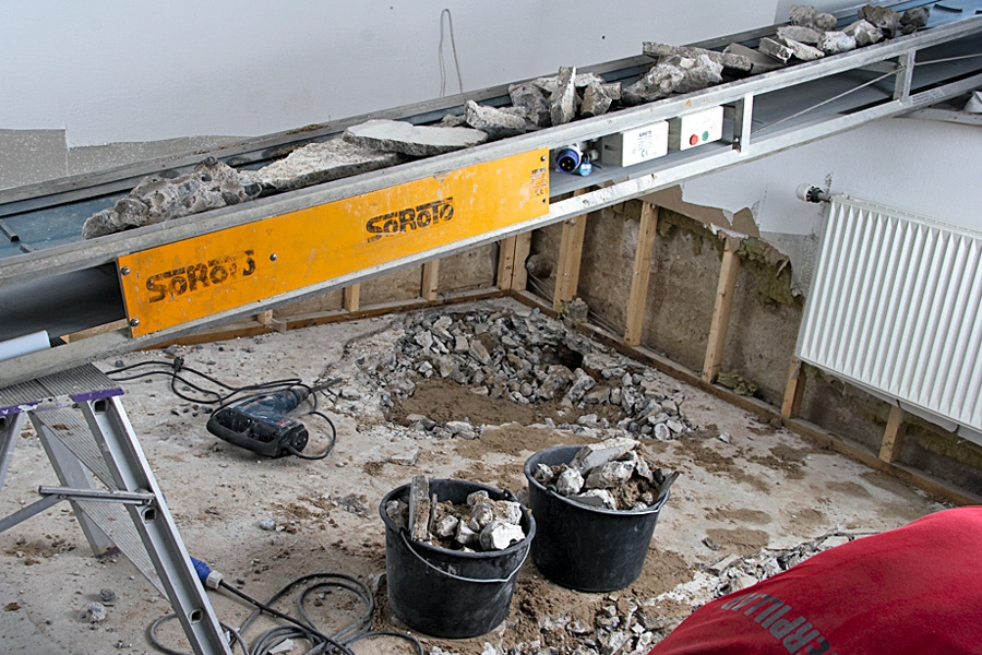 Du kan bruke hele sommerferien på å grave opp kjellergulvet og bære jord og betongrester opp gjennom trapper og entre, og videre rundt gjennom hagen – eller så kan du la transportbåndet kjøre alt gjennom vinduet og rett ut i en tilhenger.