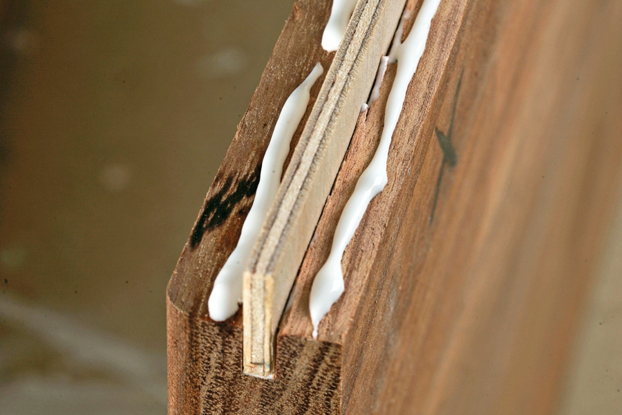 Lim en løs fer fast i noten: Feren presses ned i den ene not, hvorefter der lægges en stribe lim på pladekanten på begge sider af feren.