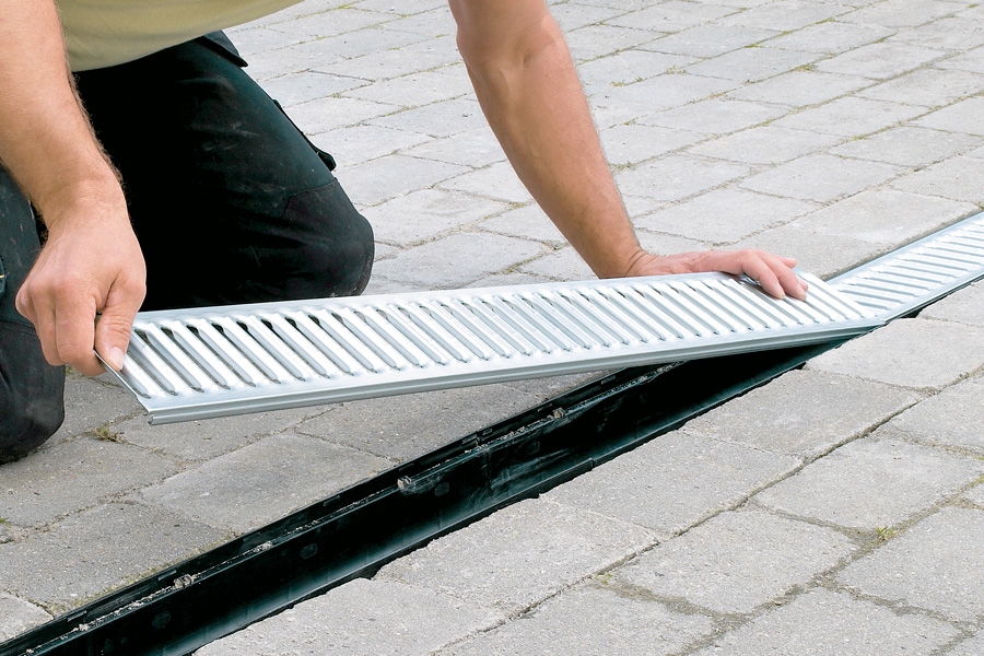 Læg risten på plads, når du har stampet stenene en smule. Når du begynder at bruge indkørslen, vil stenene synke de sidste par mm, så de kommer til at flugte med den øvrige belægning. Herefter er det bare at parkere bilen i den dejlig tørre indkørsel.