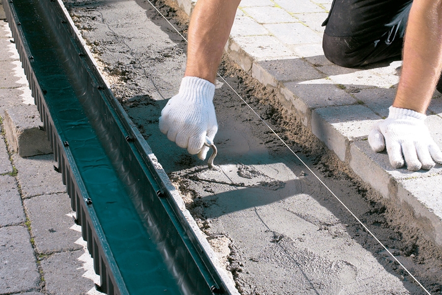 Fyld beton i udgravningen og rundt om det afløbsrør, tuden skal placeres i. Betonen glattes ca. 8 cm under belægningens overflade. Vi blander betonen af en del cement, tre dele støbemix og en lille smule vand.