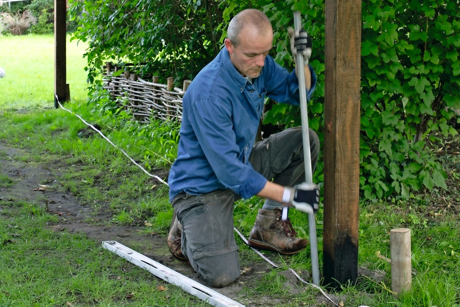 Om stolparna bara ska stå i marken, grävs de 4 hörnhålen och stolparna ställs ner på ett lager sand eller småsten. Jord packas runt om stolparna, 20 cm åt gången, och man kollar så att de står i lod.