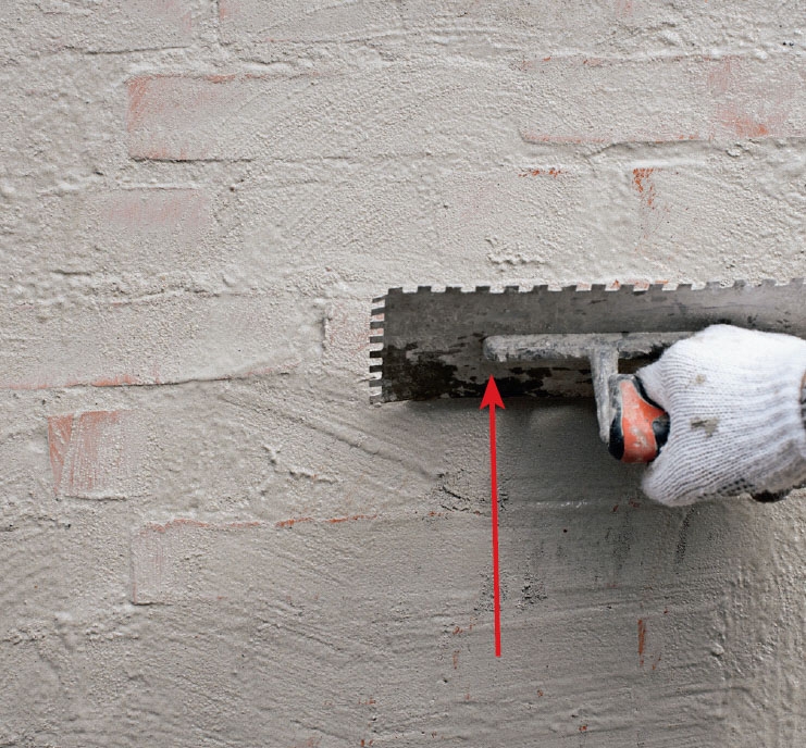 Tiiliseinän rappaus: Osa laastista raavitaan pois teräs-lastan reunalla