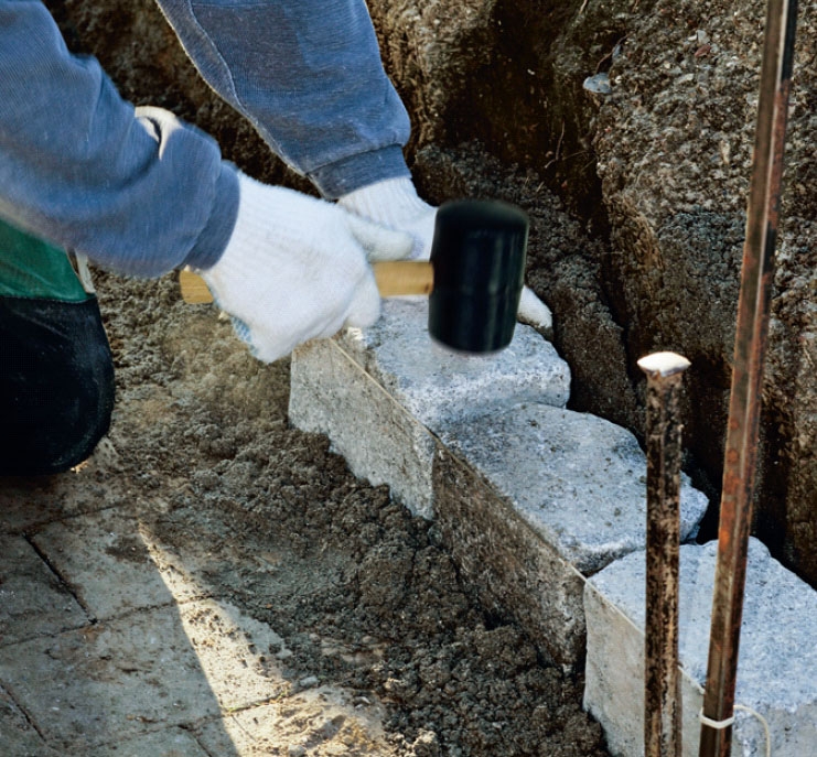 Snygg mur av gatsten: Banka stenarna på plats med en gummihammare