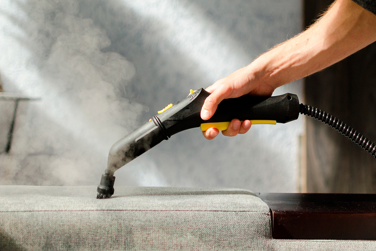 Käsi puhdistamassa sohvaa höyrypesurilla.