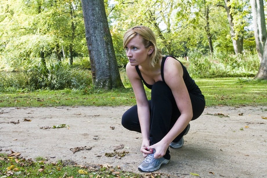 Kvinna sitter på huk och knyter sina löparskor