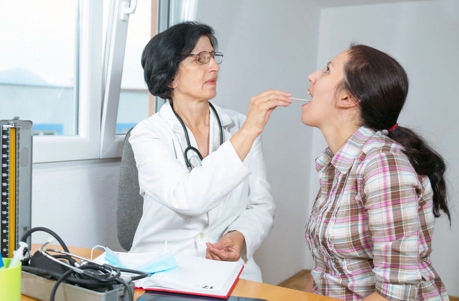 Halsbetennelse - kvinne med vondt i halsen sjekkes hos legen