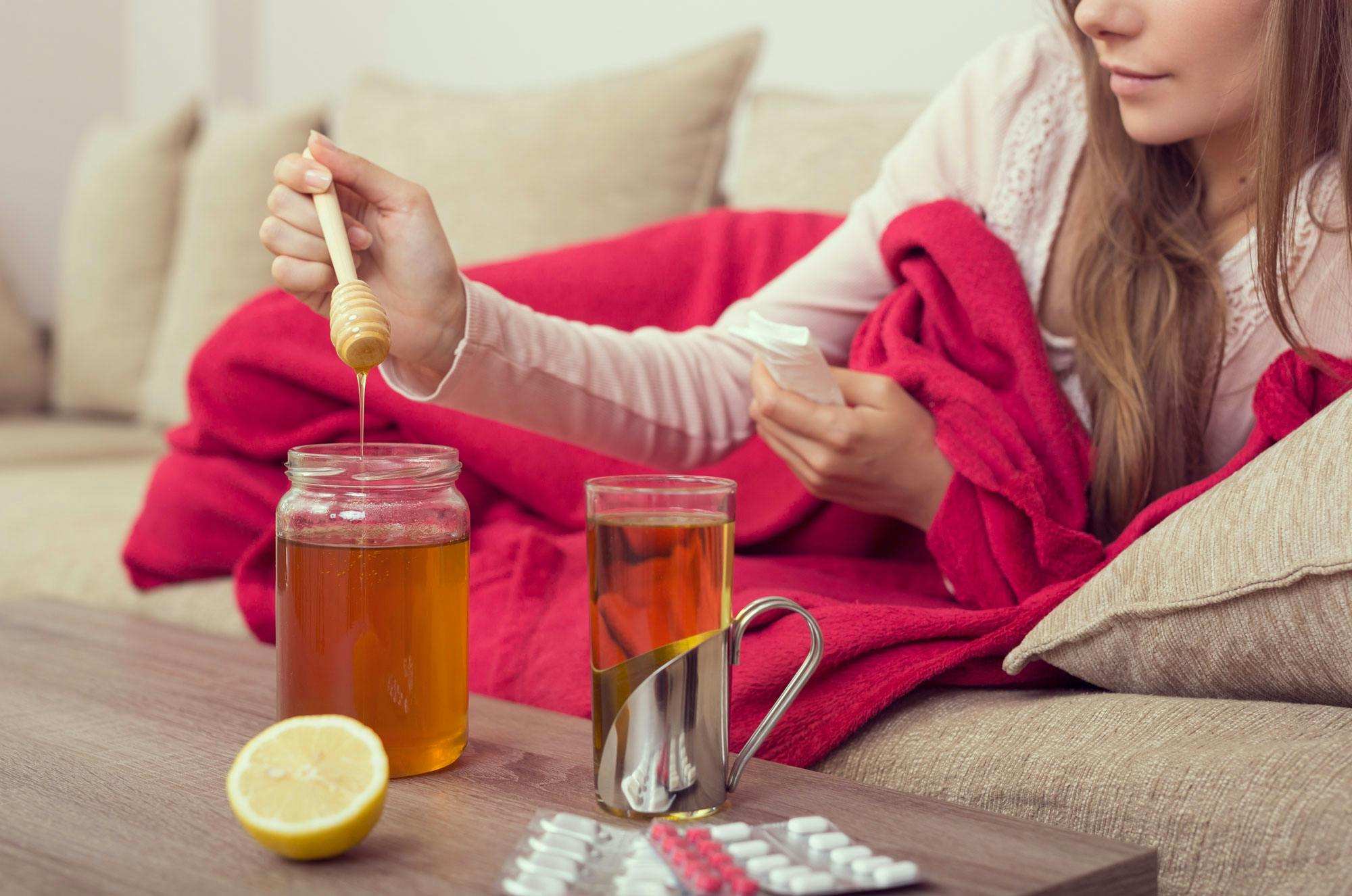 Kvinde med halsbetændelse hviler i sofa med varm te med honning og citron