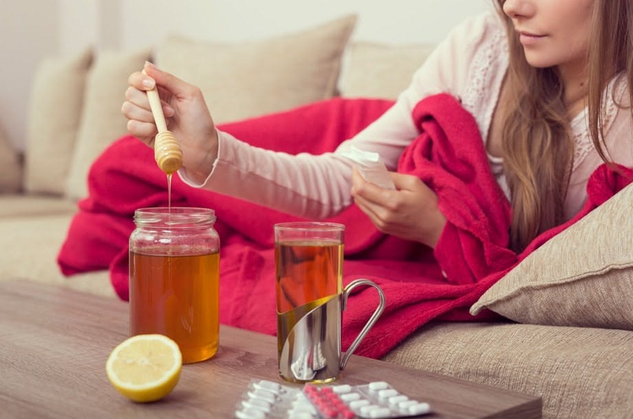 Kurkkutulehdusta sairastava nainen laittaa hunajaa teehen.