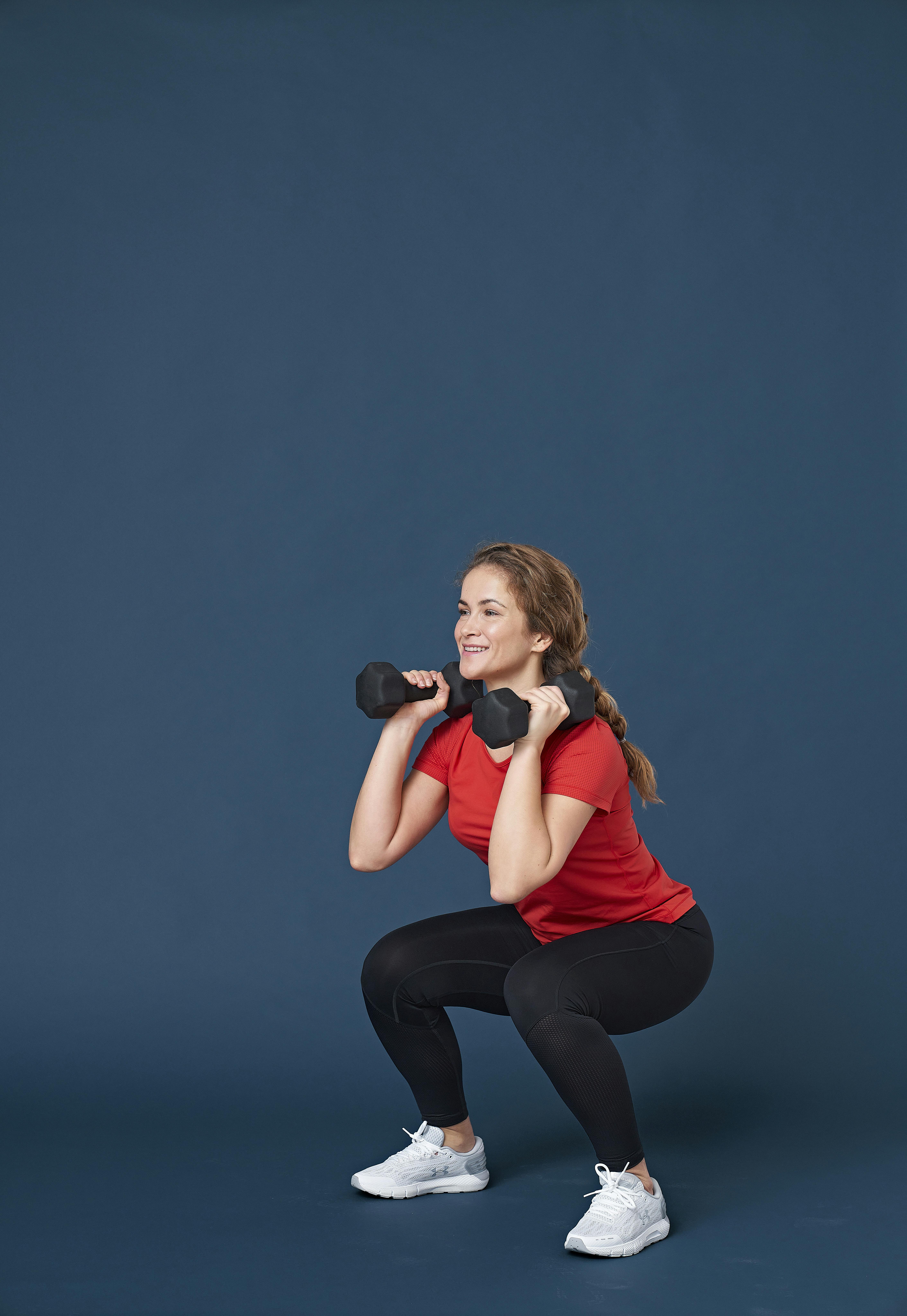 Nainen kyykkää käsipainot käsissä