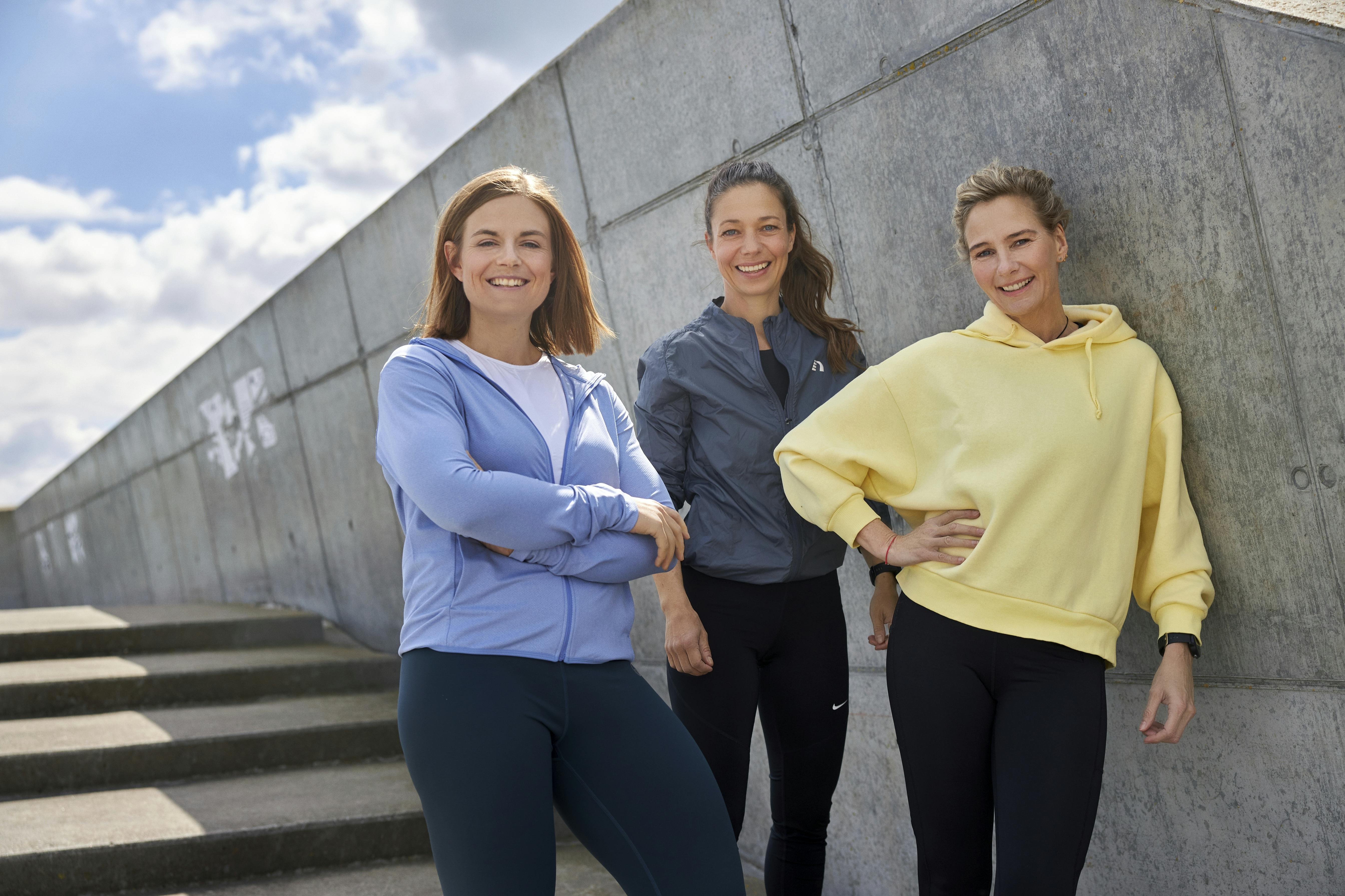 Tre kvinner i sportsklær står mot veggen