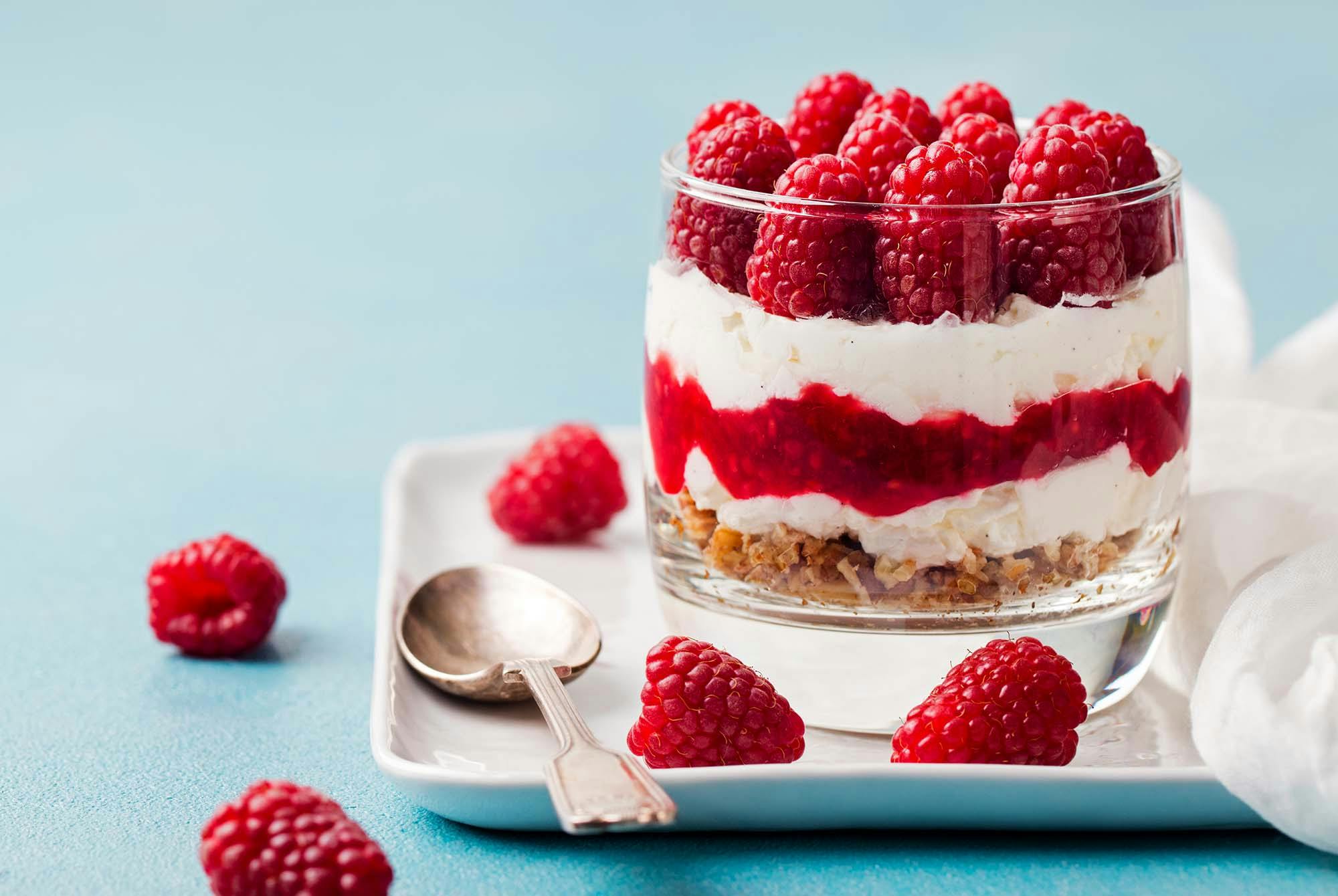 Vadelmia jälkiruoka-astiassa vaaleaa taustaa vasten