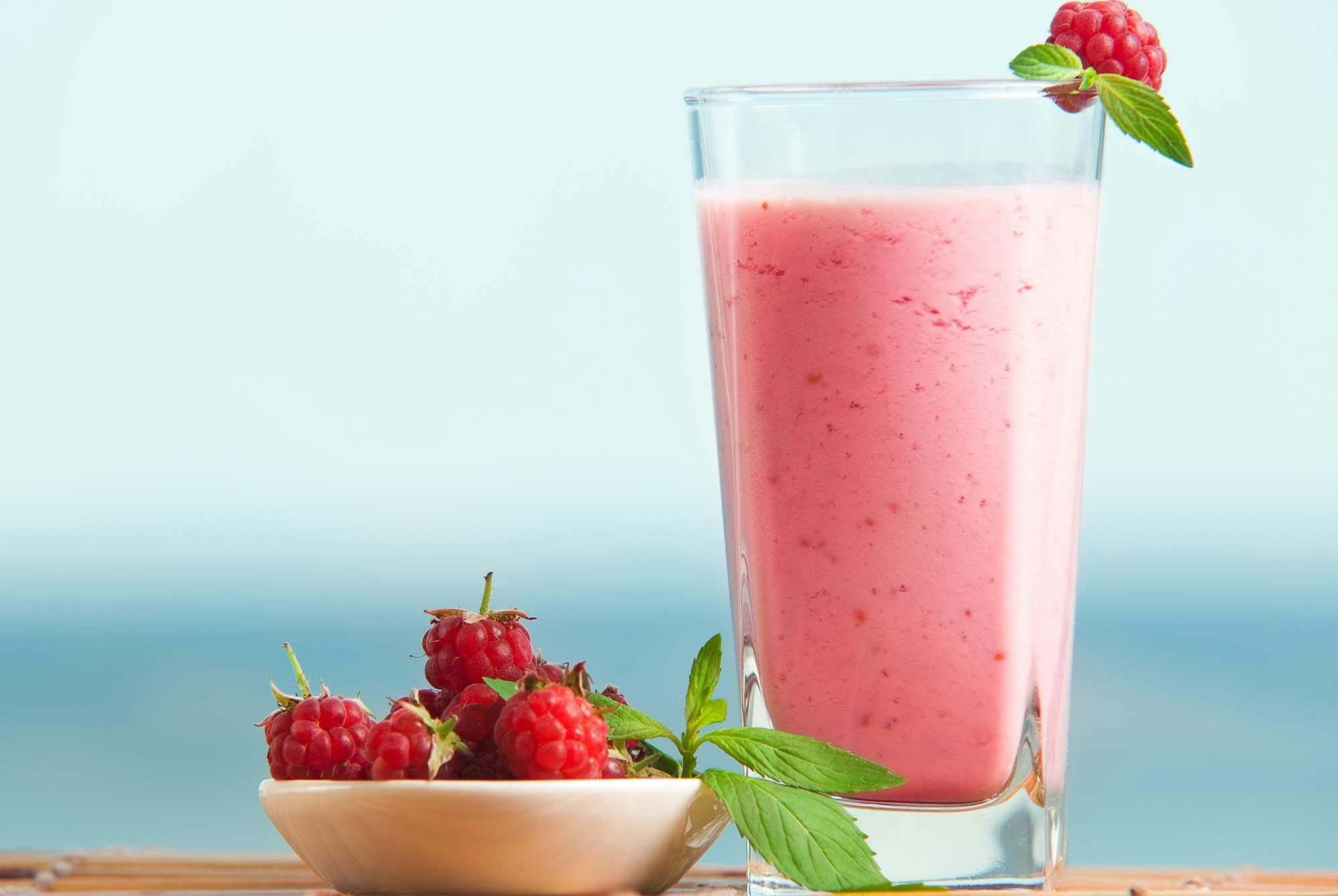 Vadelmasmoothie lasissa, jonka vieressä vadelmia kulhossa