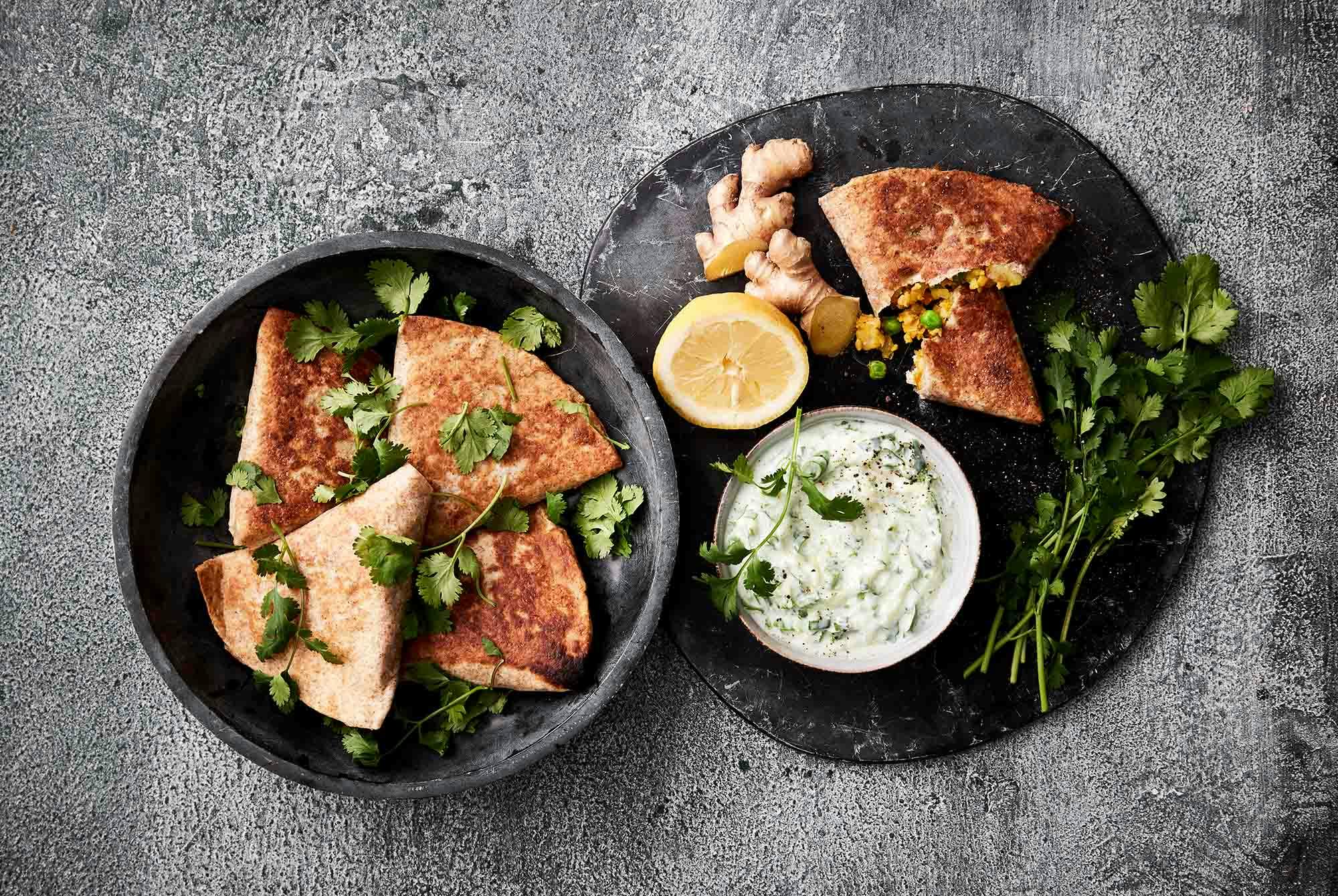 Samosas på sort fad med koriander drysset oven på
