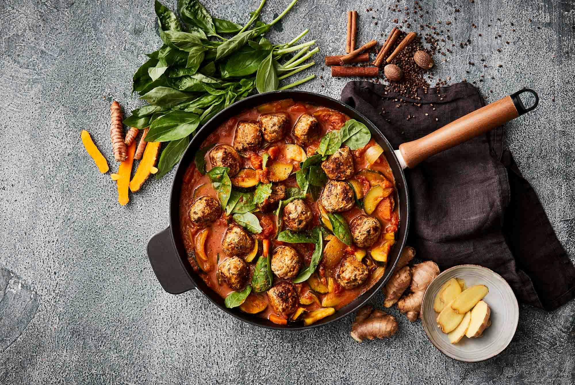 En skål med en röd sås med grönsaker, spenat och köttbullar på toppen