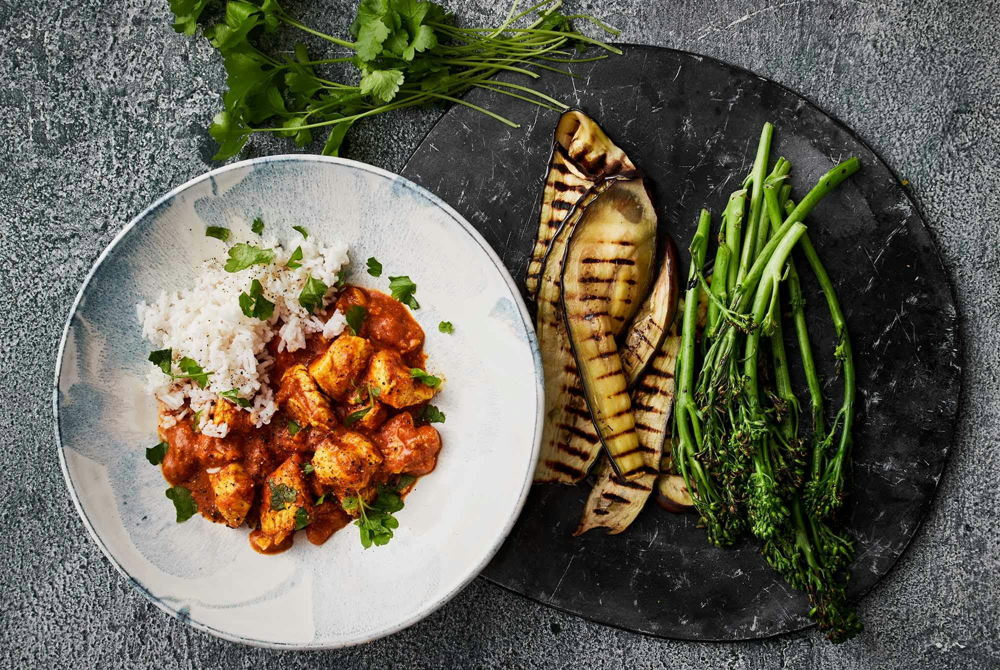 En hvid tallerken med ris, butter chicken og frisk koriander drysset oven på.
