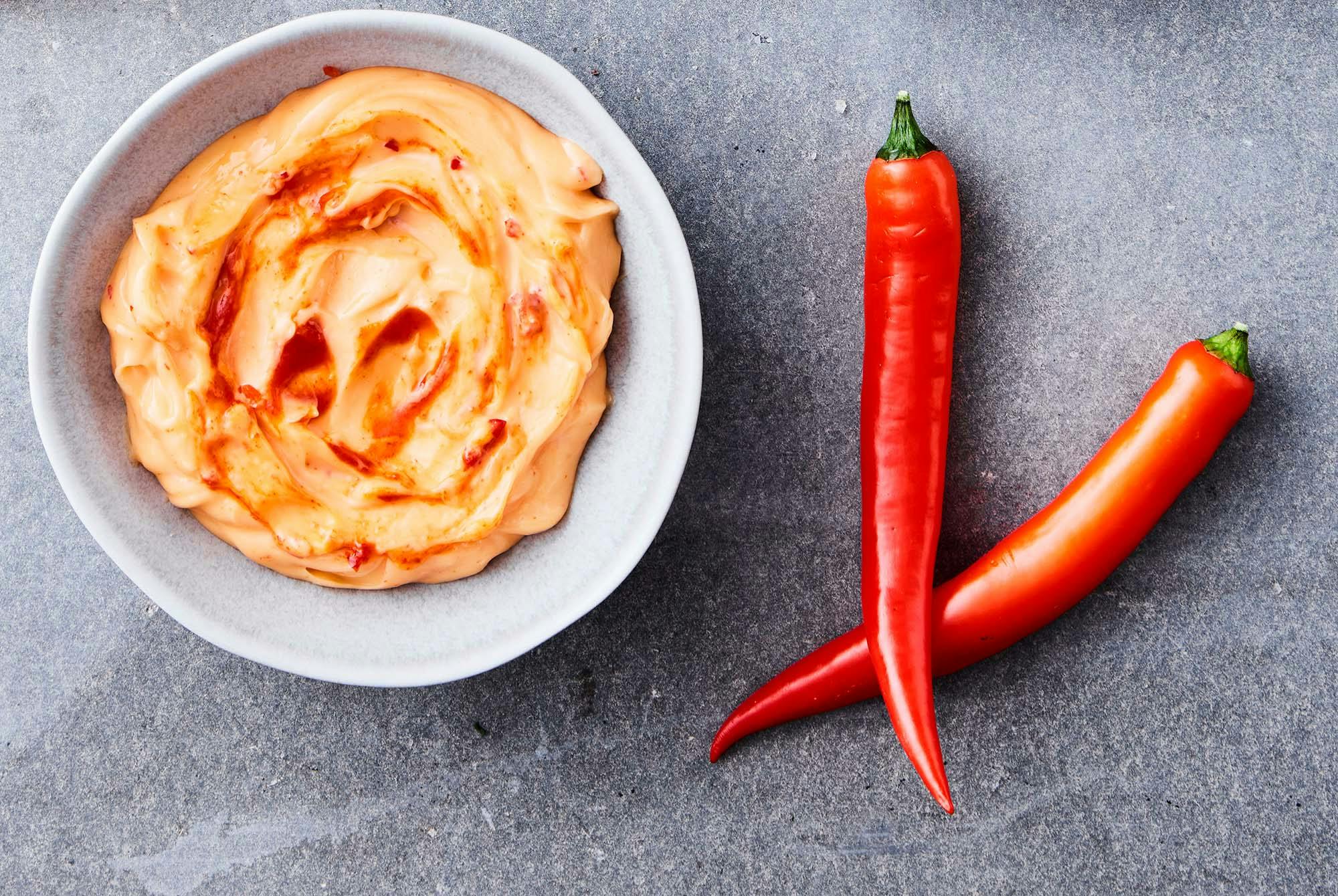 Kulho chilimajoneesia ja vieressä kaksi chilipaprikaa