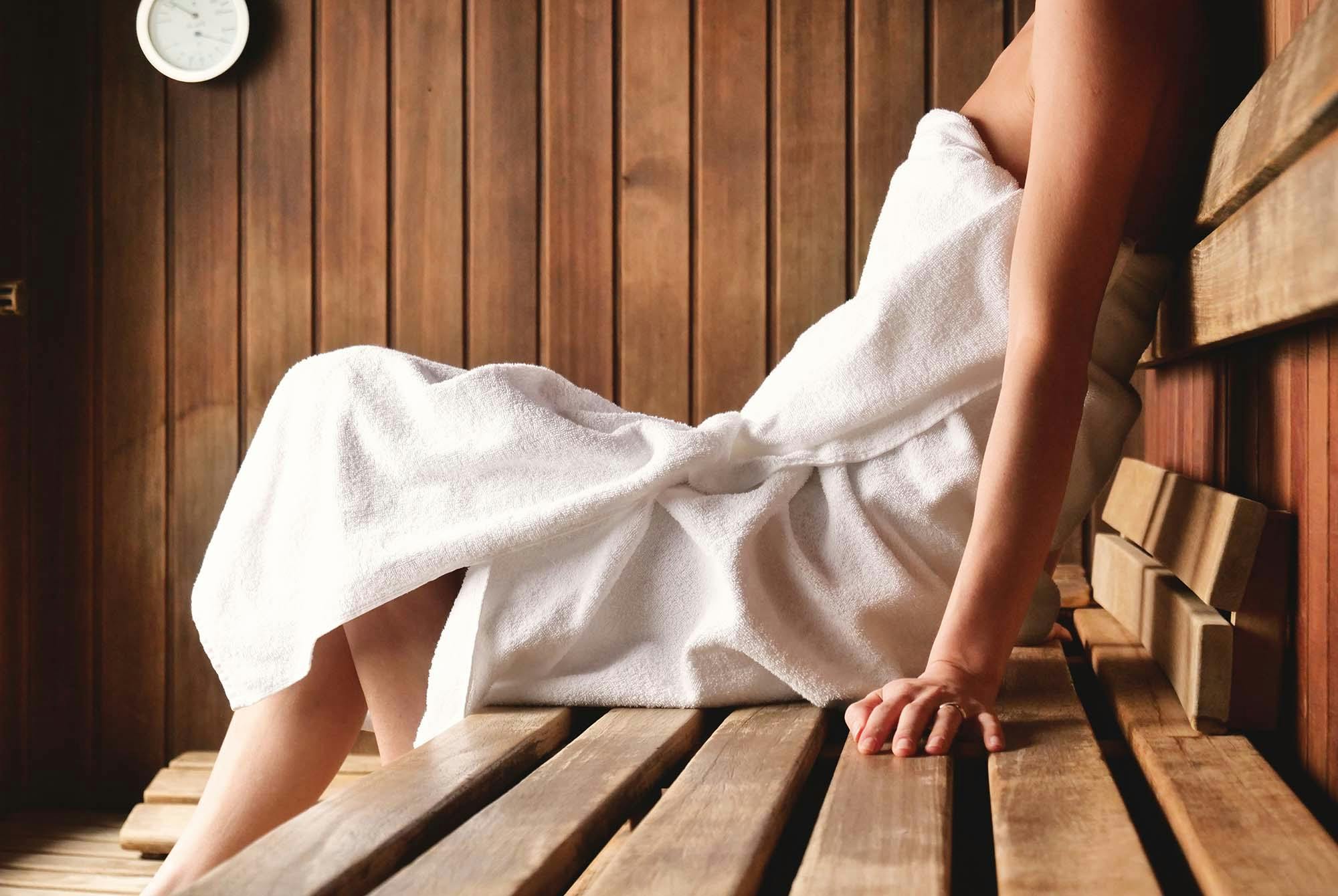 Nainen pyyhe ympärillään saunan lauteilla - sauna on hyväksi keholle ja mielelle