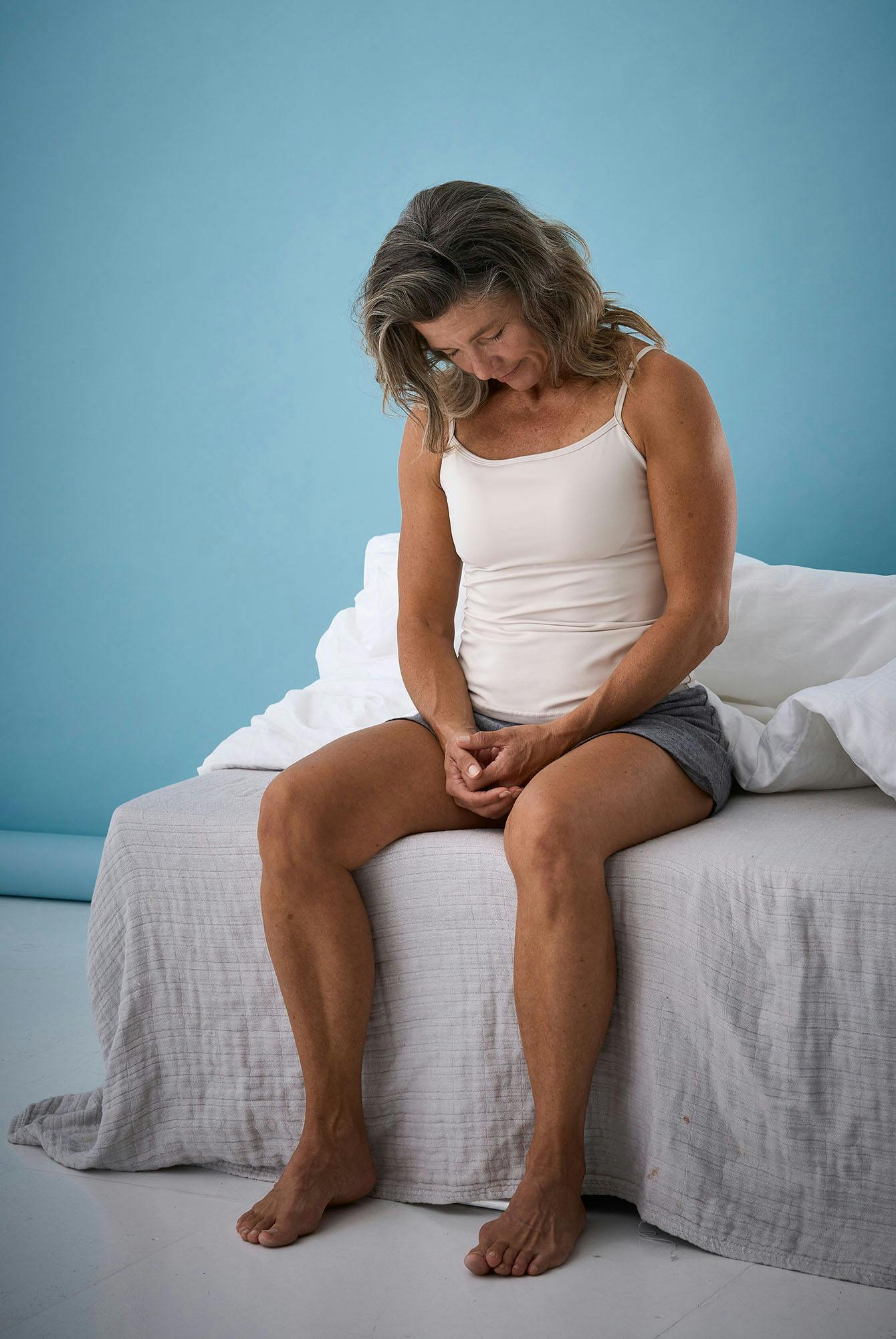 Kvinne sitter på sengekanten og ruller med hodet